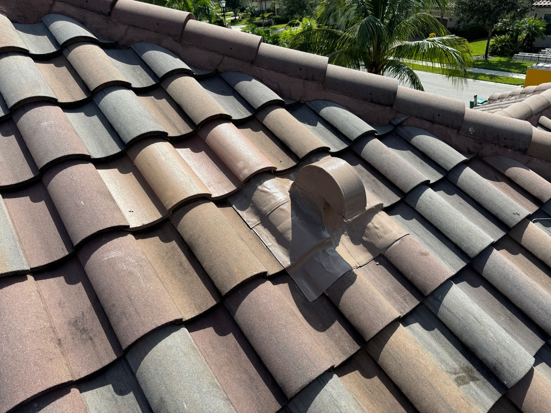Close-up of a tiled roof. A rolled piece of gray tape secures a broken tile. Sunlight.