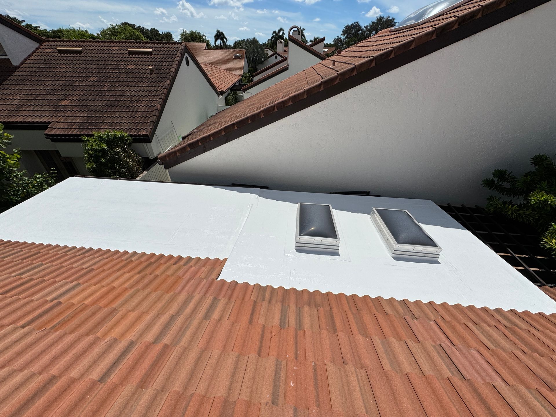 Flat white roof section with skylights, on top of red tile roof, buildings in background.