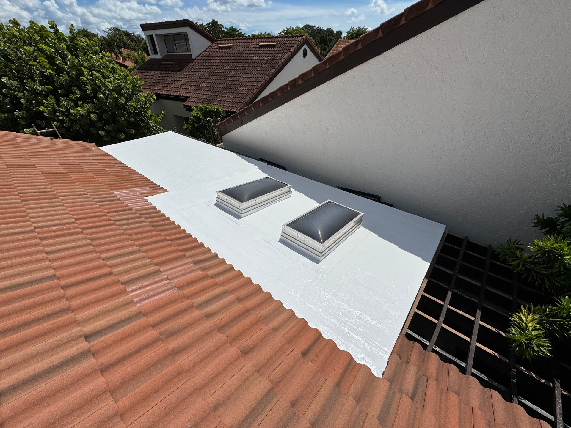View of a white flat roof with two skylights, adjacent to a red tile roof, and a white stucco wall.