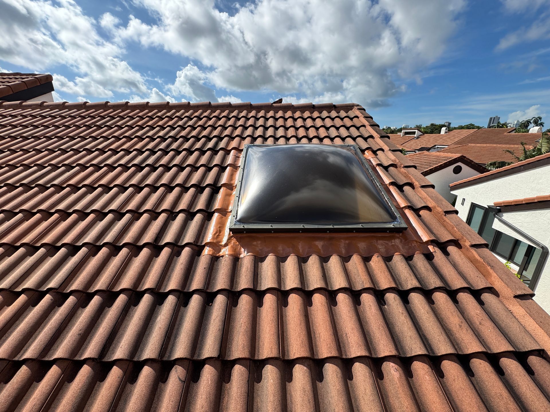 Red tile roof with a skylight, blue sky with clouds in the background.