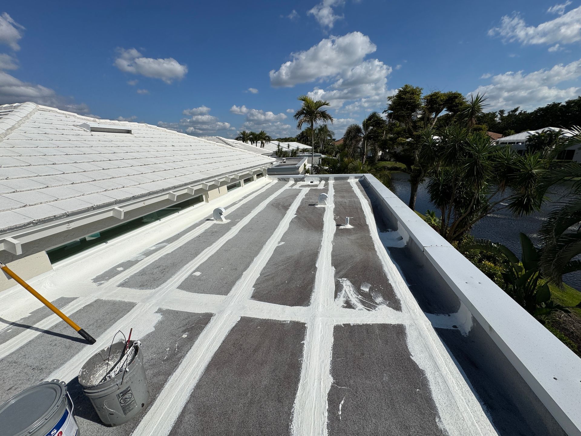White painted flat roof with linear gray sections, blue sky, bucket of paint, brush.