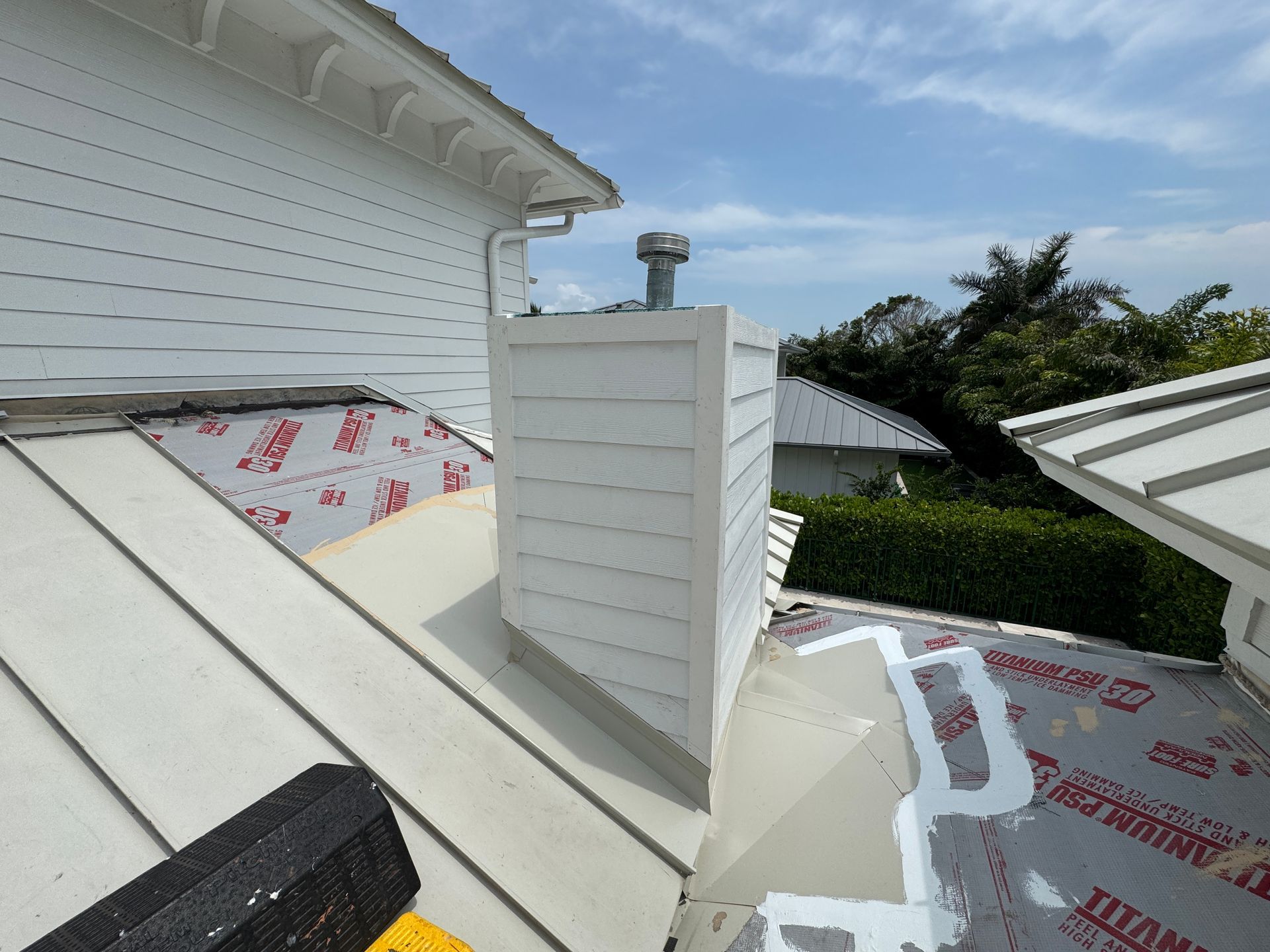 White-sided chimney on a metal roof, with partial roofing in view, under a partly cloudy sky.