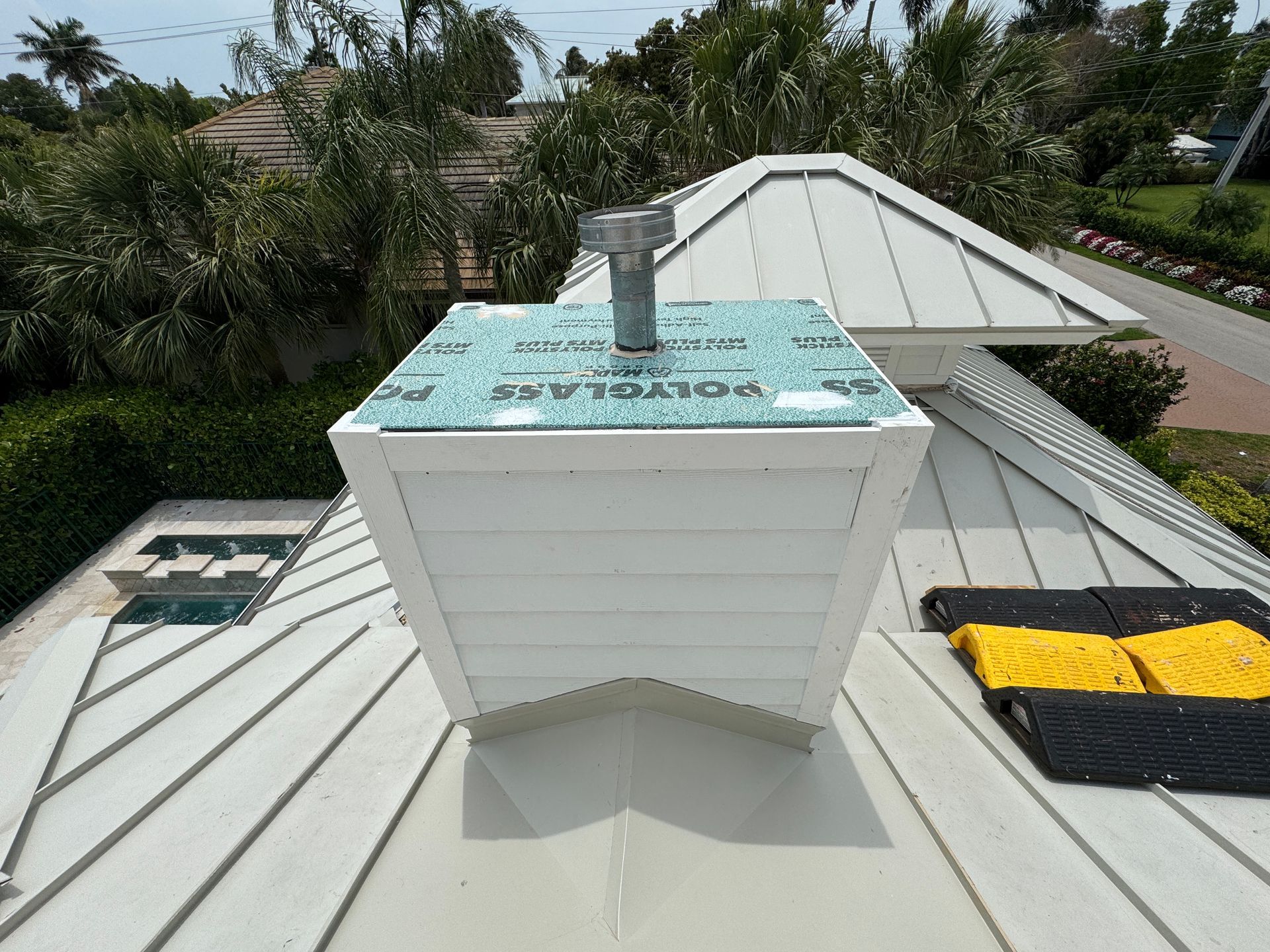 White chimney on a metal roof, with vent pipe and blue flashing.