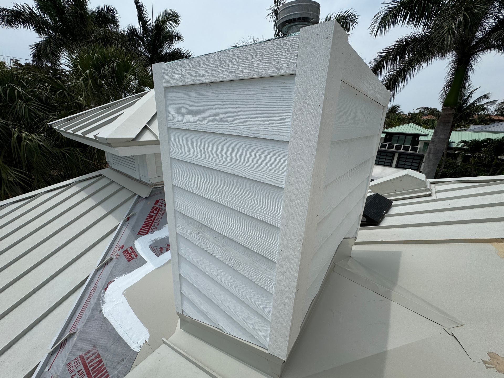 White chimney on a metal roof, angled siding, palm trees in background.