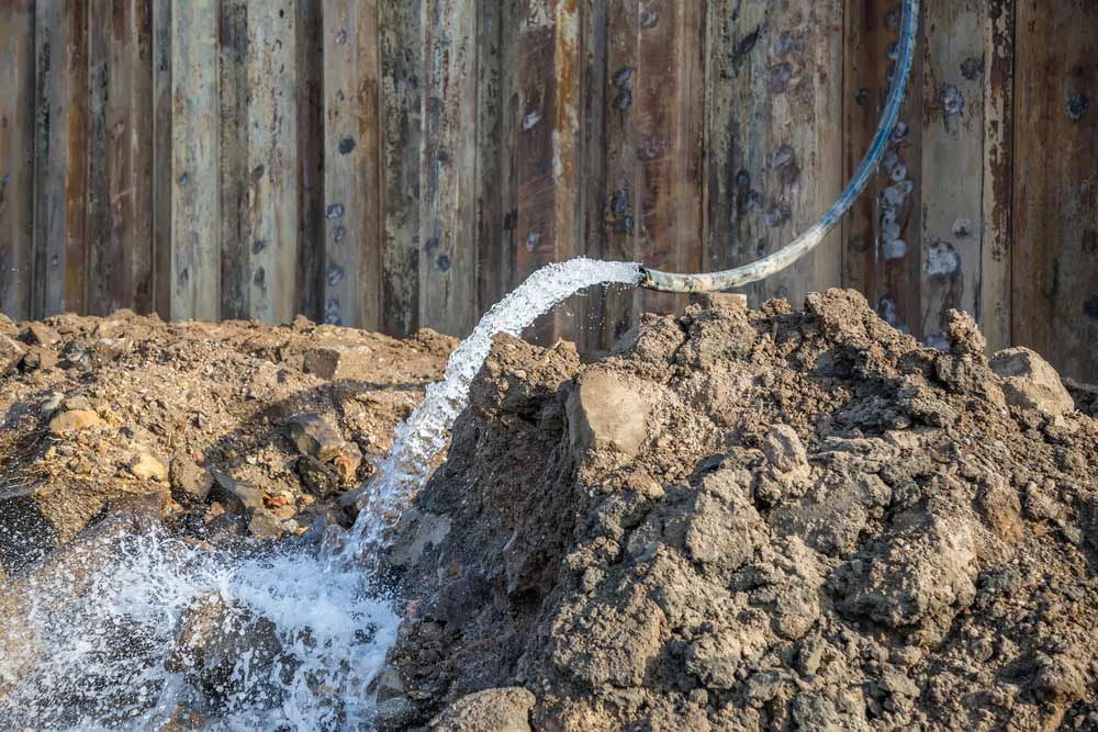 Water Spraying From a Hose Onto a Pile of Dirt, Next to a Wooden Wall — Keyeng in Slade Point, QLD