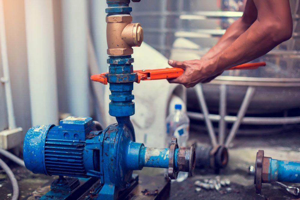 A Person Using a Wrench to Repair a Blue Water Pump — Keyeng in Slade Point, QLD