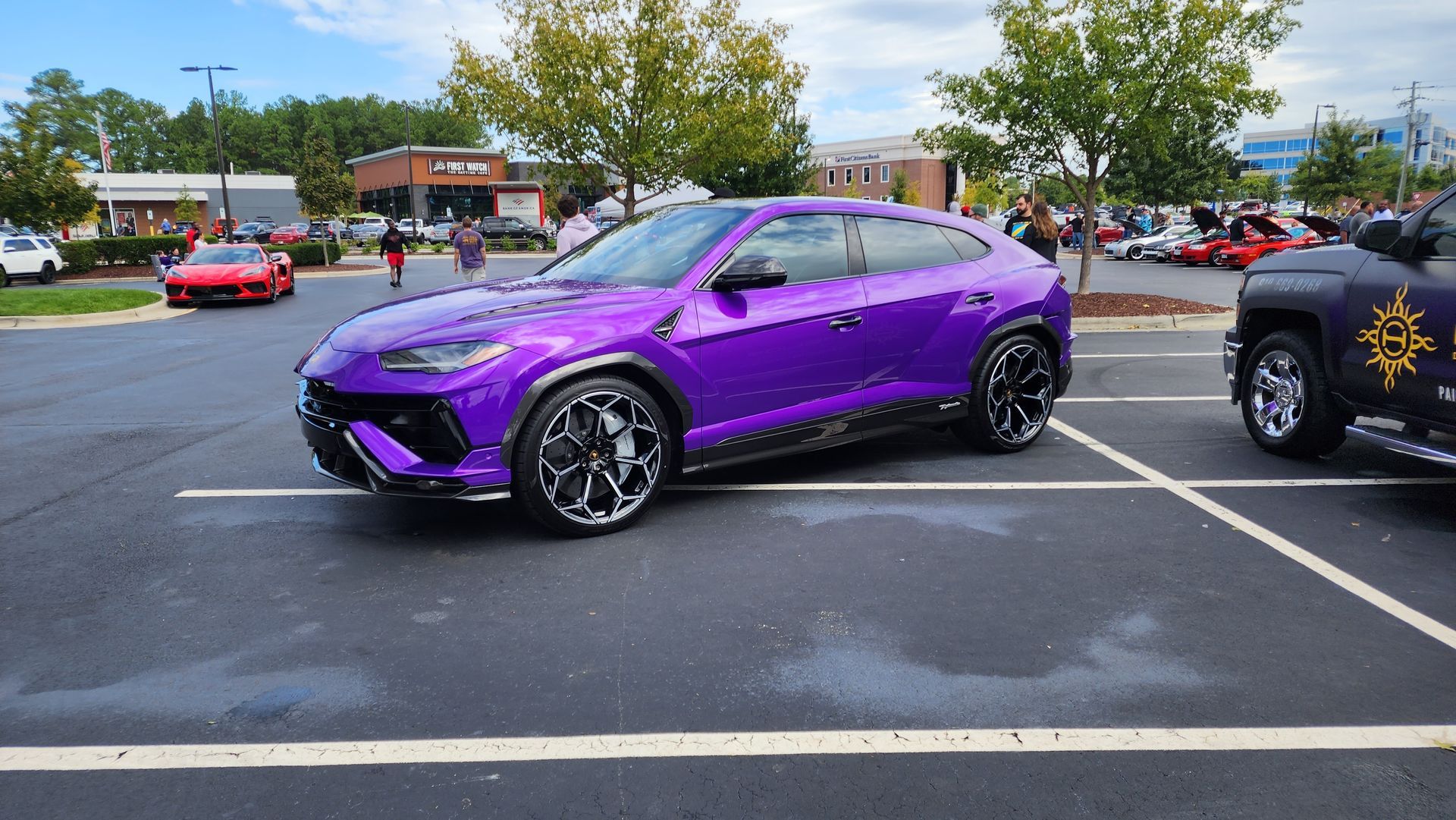 Purple Lamborghini SUV parked in a lot. People in the background.