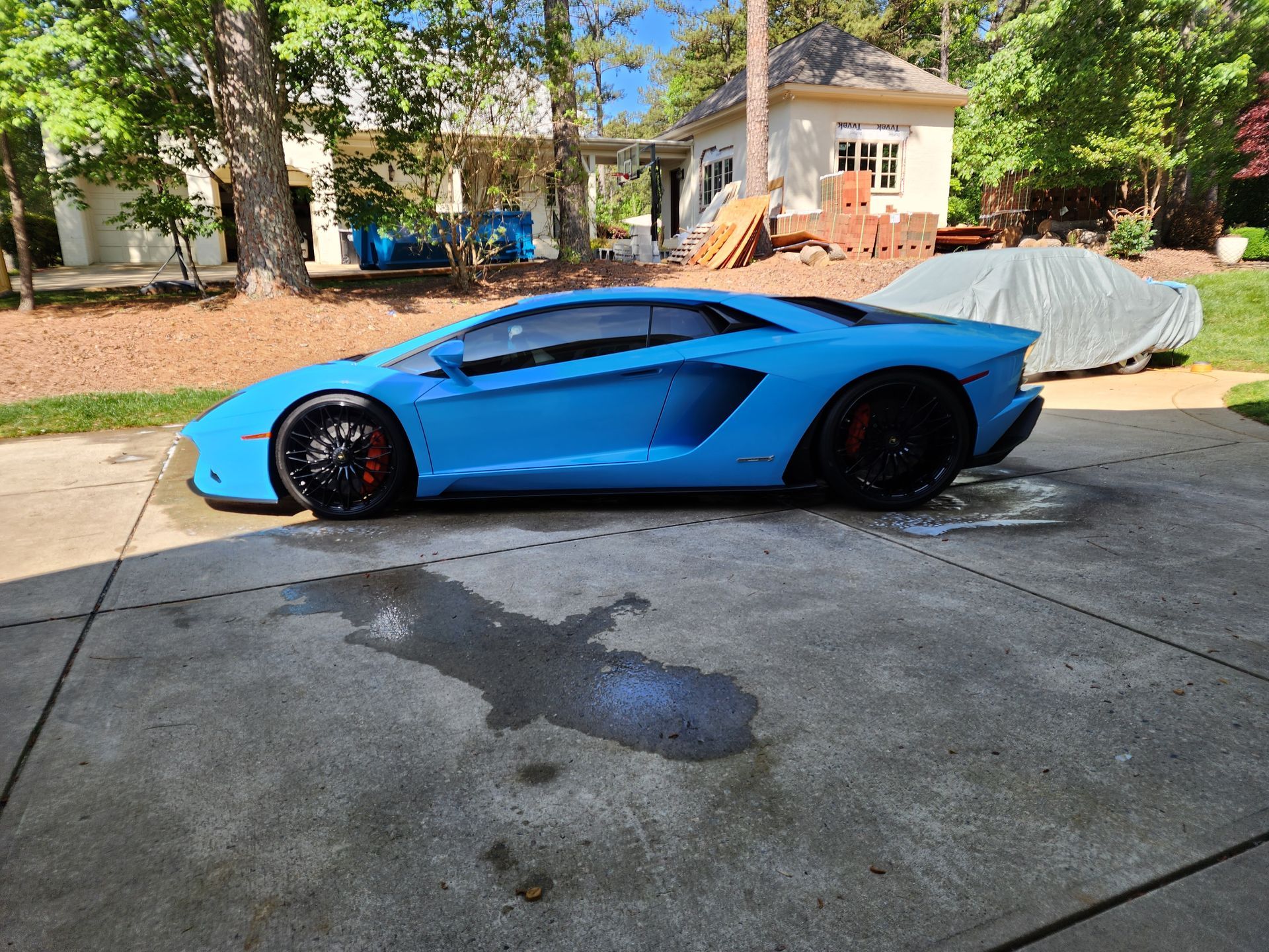 A blue lamborghini aventador is parked in a driveway next to a house.