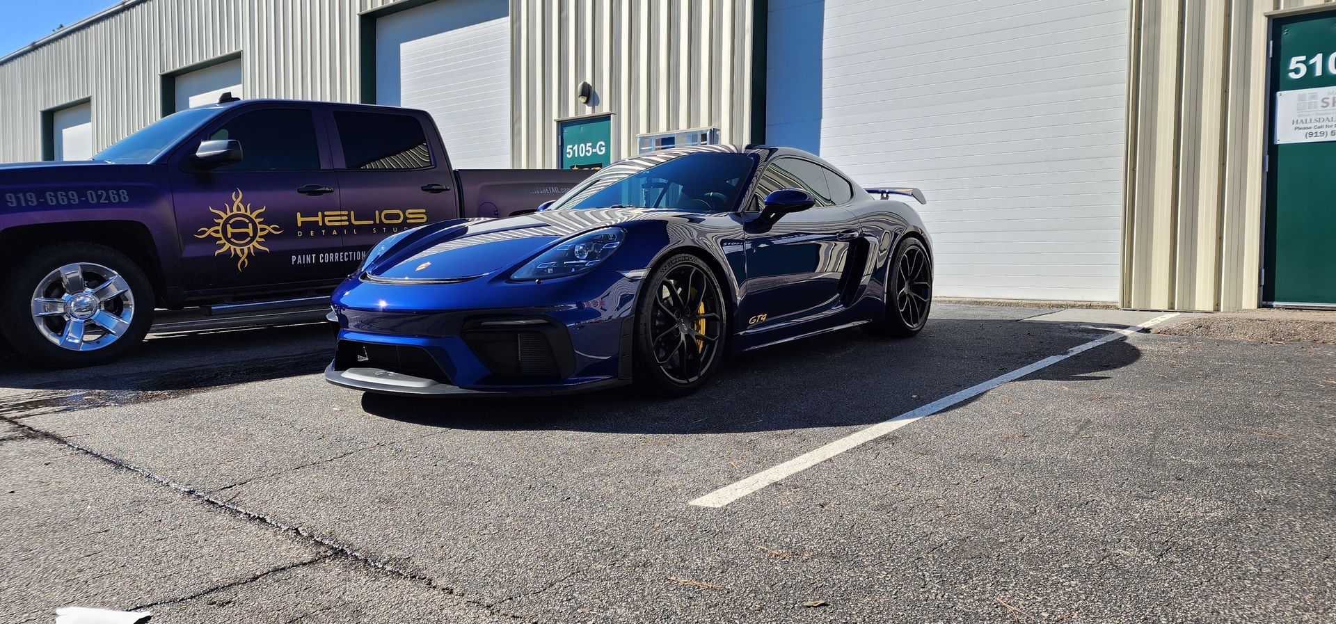 A blue sports car is parked in a parking lot next to a truck.