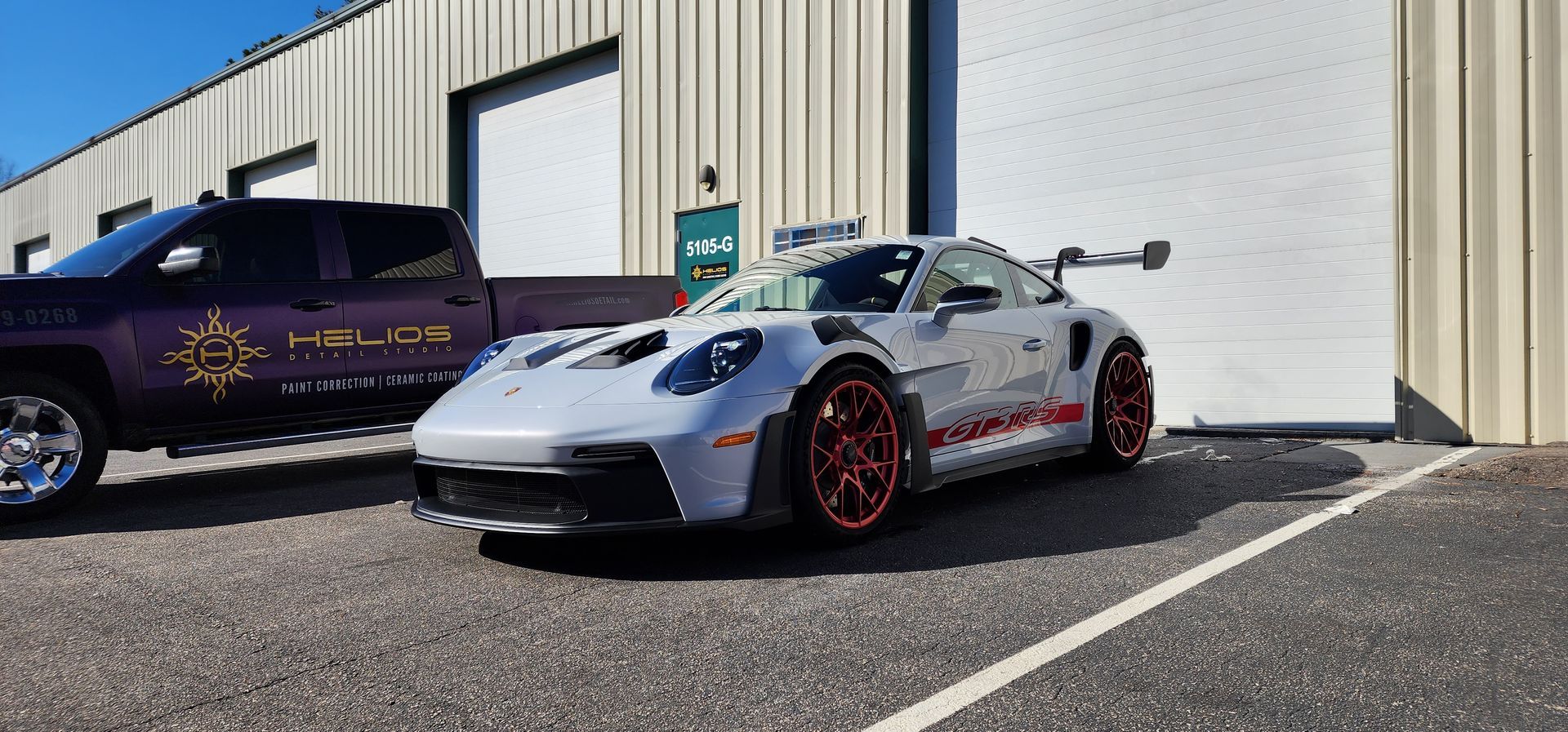 A silver Porsche 911 GT3 RS is parked in a parking lot next to a truck.