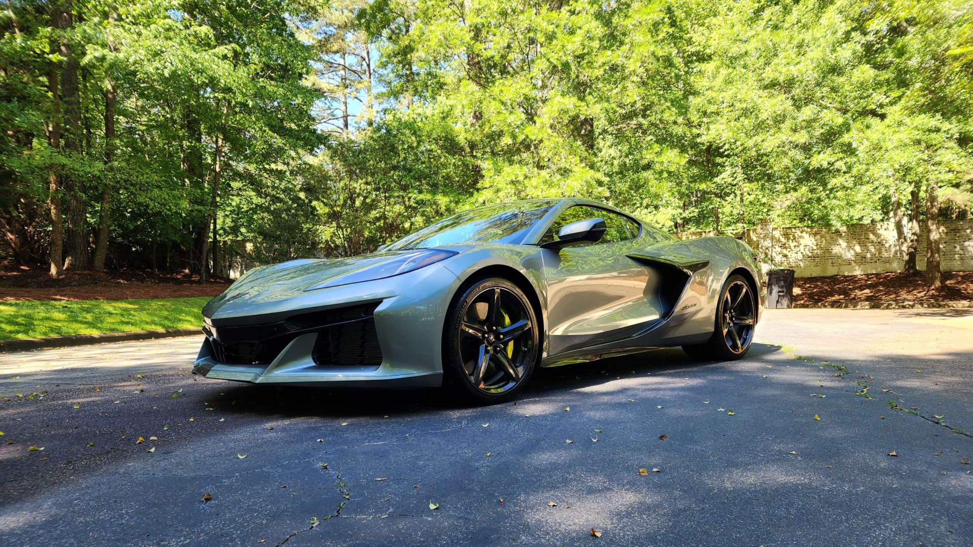 Silver sports car parked on a driveway with trees in the background.