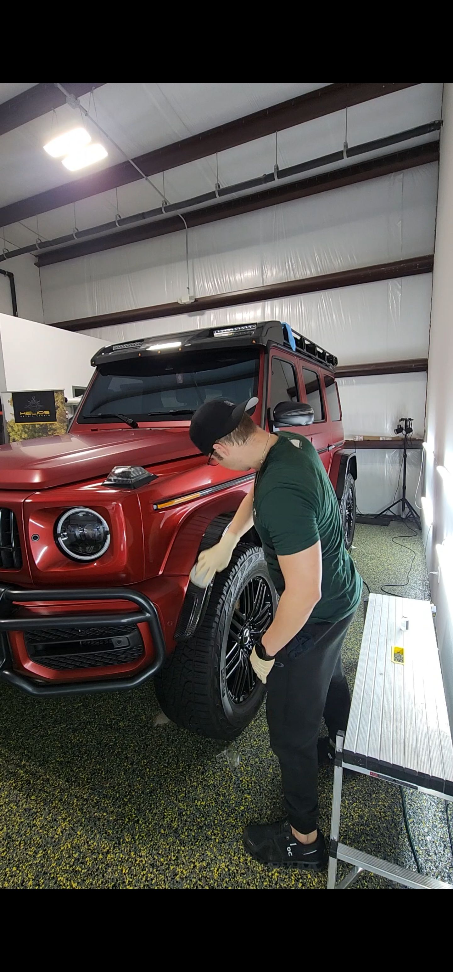 Person standing beside a red SUV in a garage, reaching toward the vehicle's front wheel area.