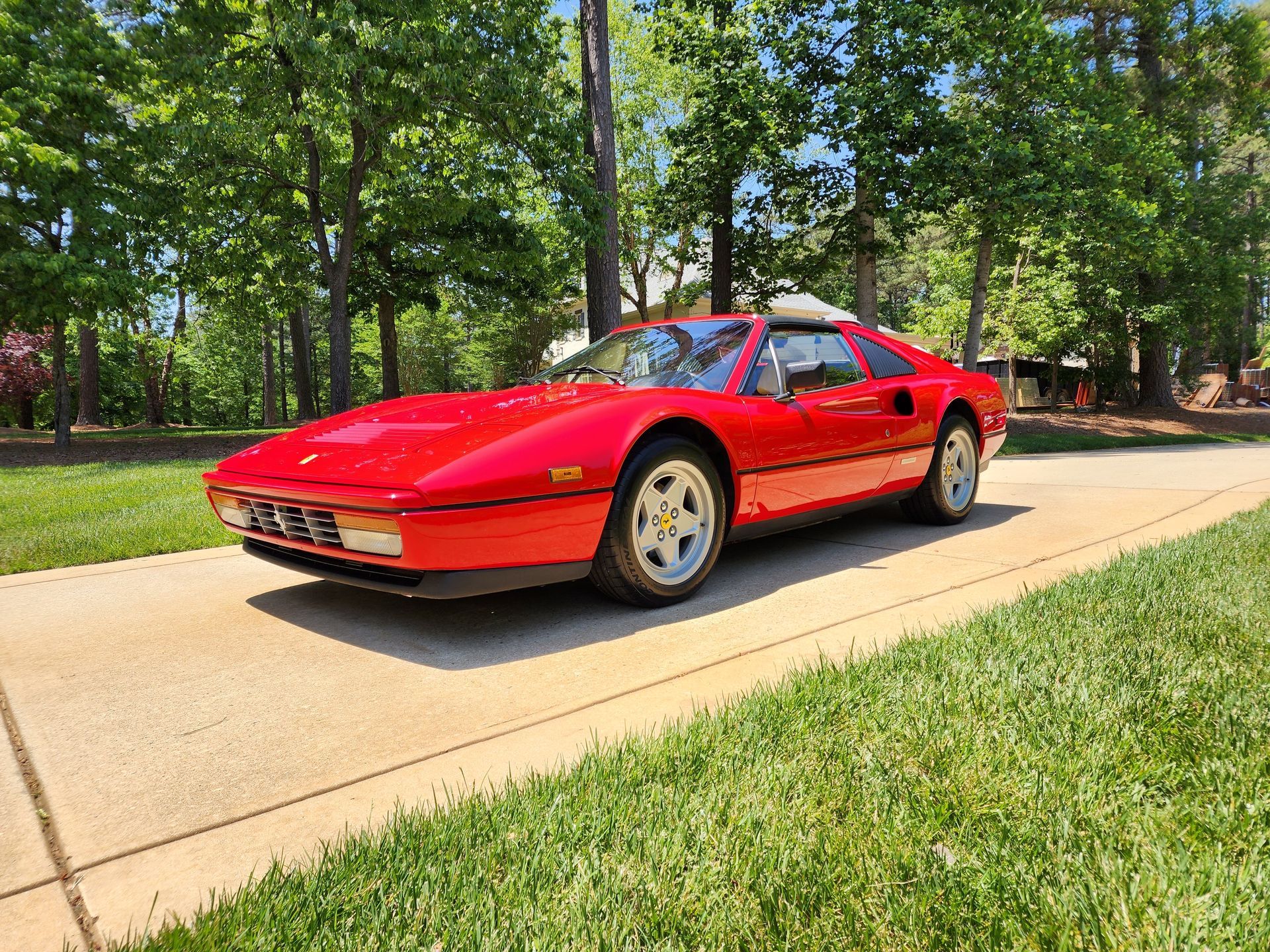 Red Ferrari sports car on a concrete driveway, surrounded by green grass and trees.