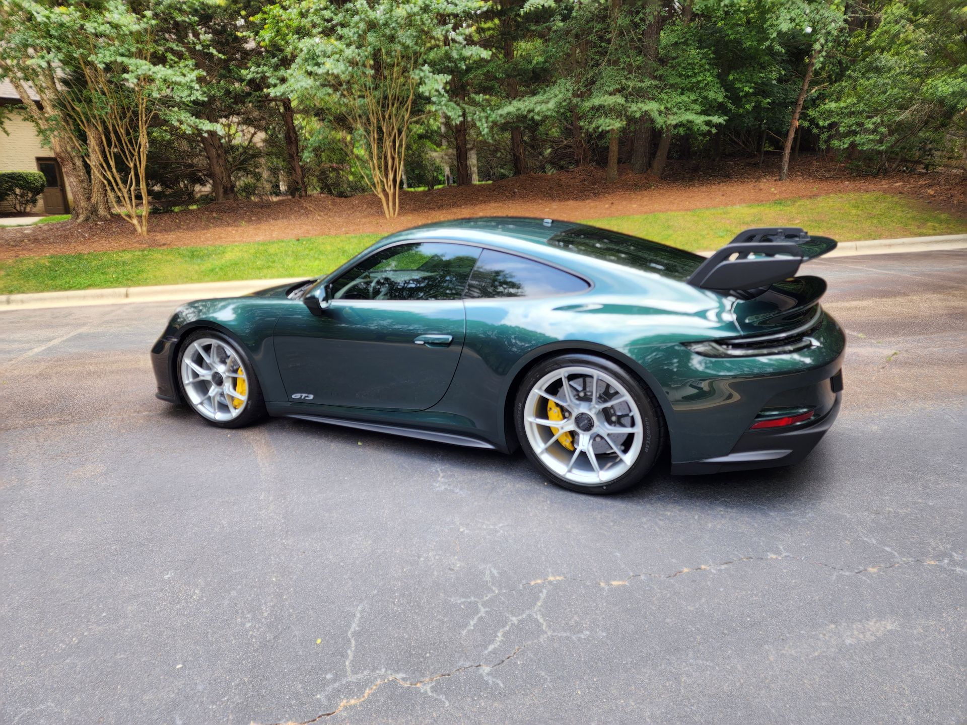 Green Porsche sports car parked on asphalt, yellow brake calipers, large rear wing.