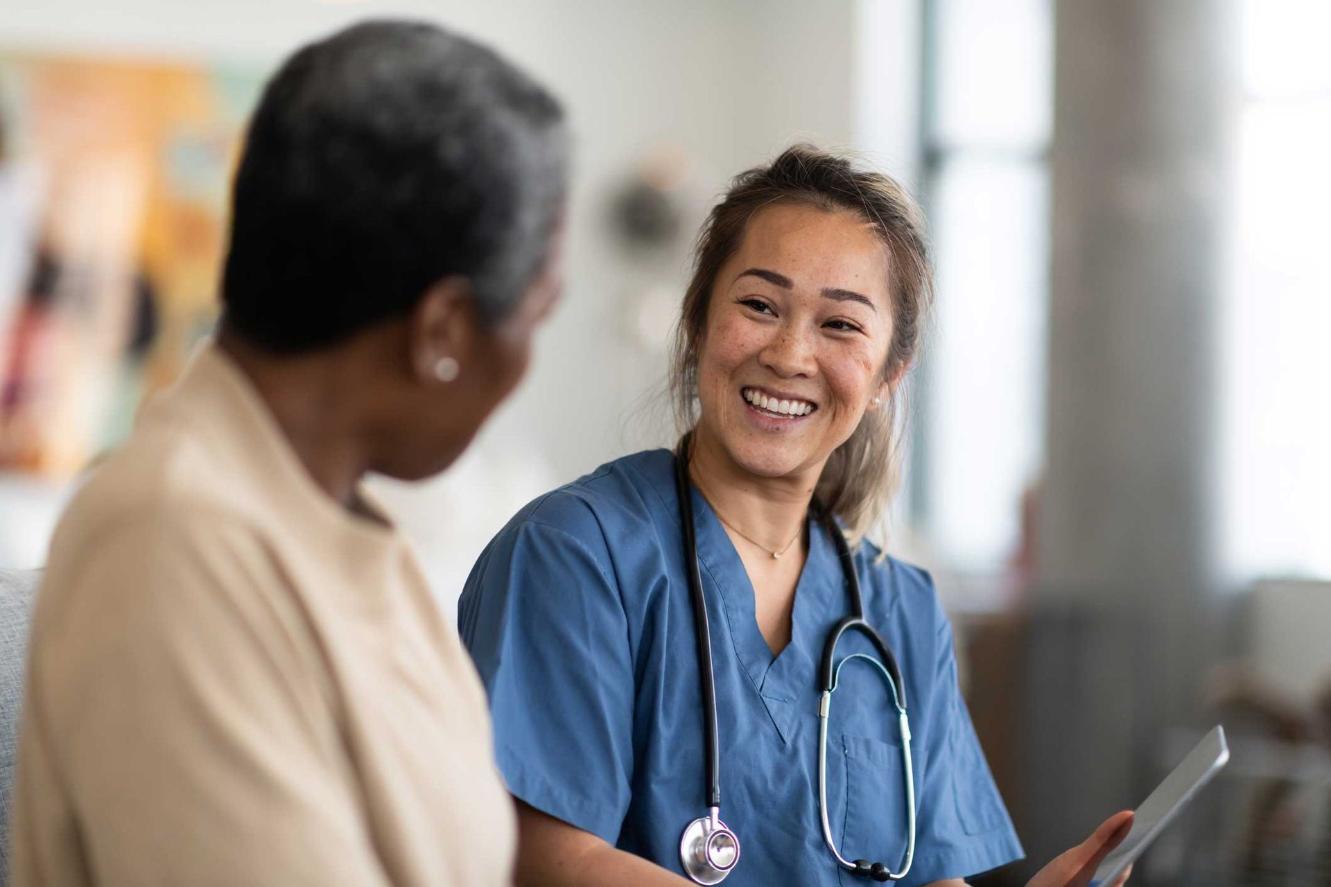 A nurse is talking to an older woman while holding a tablet.
