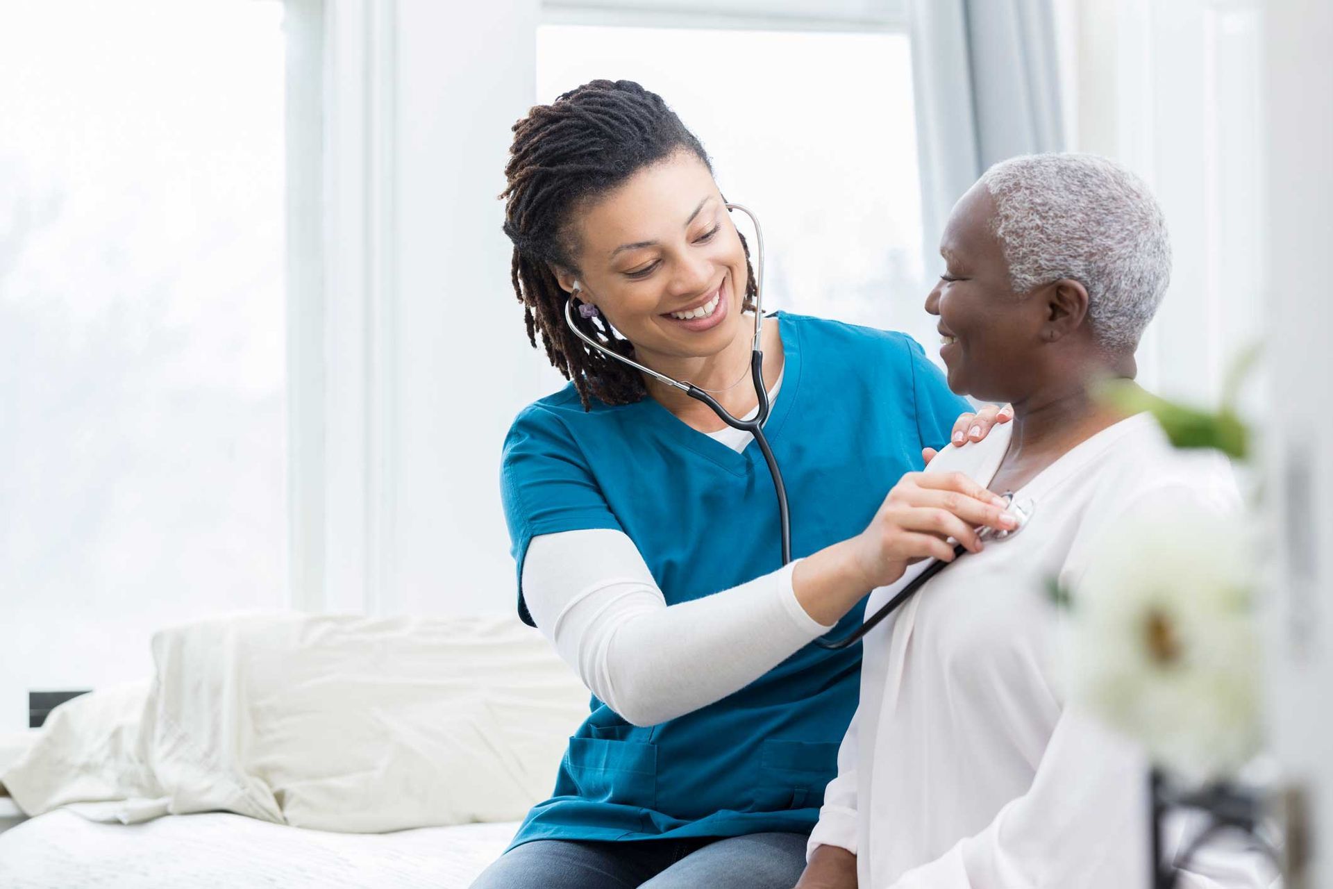 A nurse is listening to an older woman 's heartbeat with a stethoscope.
