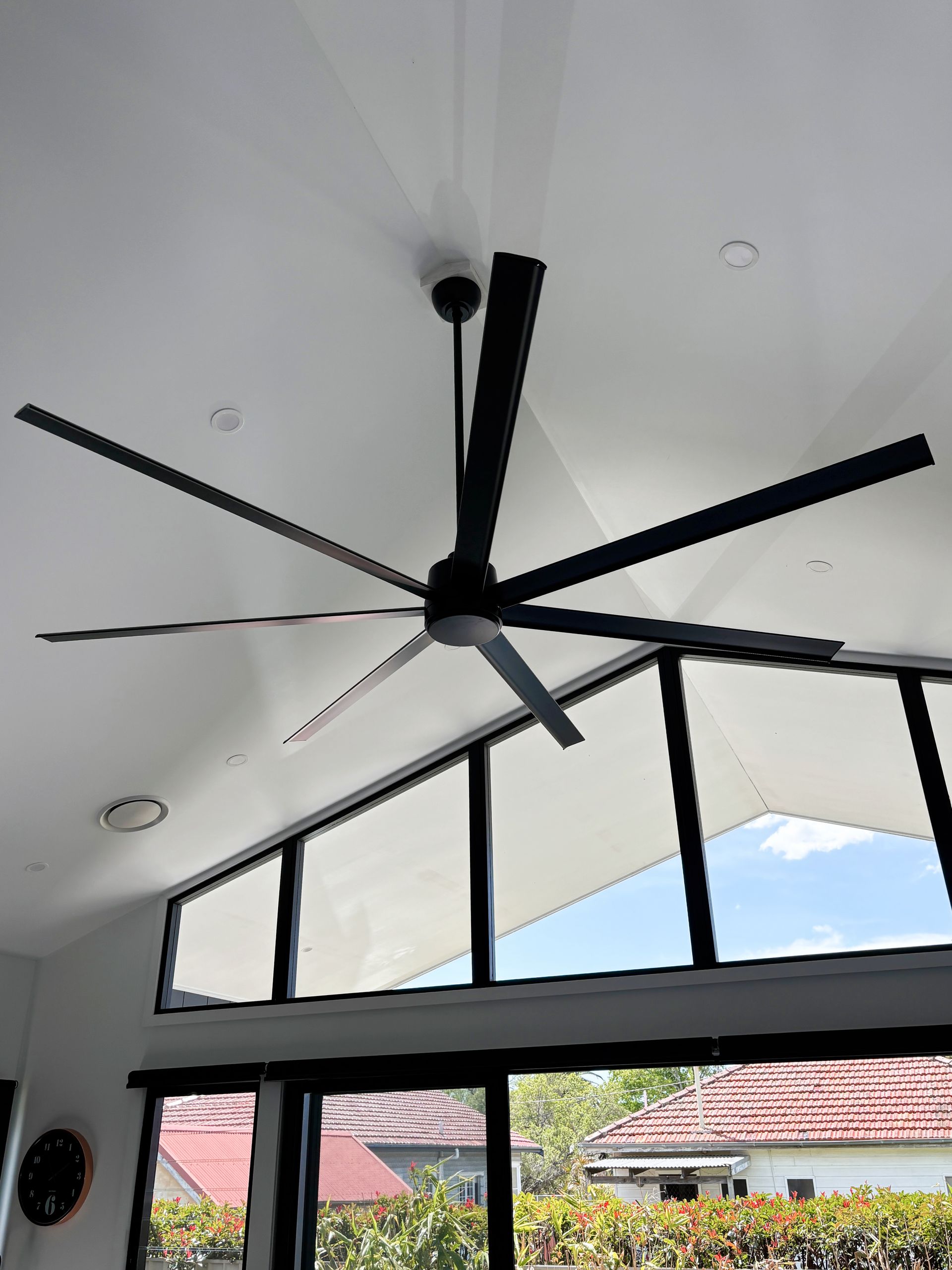 A large ceiling fan is hanging from the ceiling of a room with lots of windows.