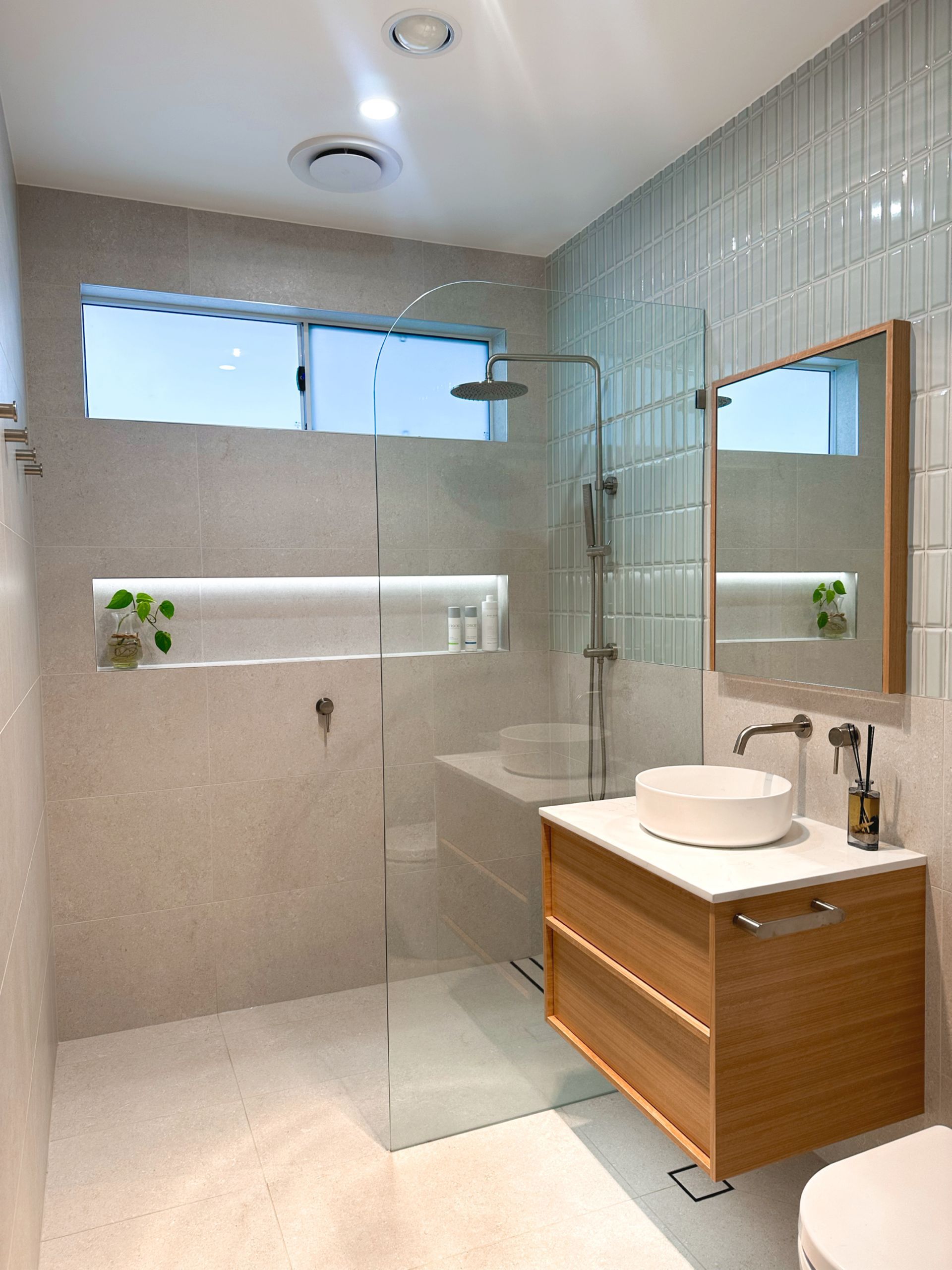 A bathroom with a sink , toilet , shower and mirror with LED lighting in the wall niche, down lights, heat lighting. 