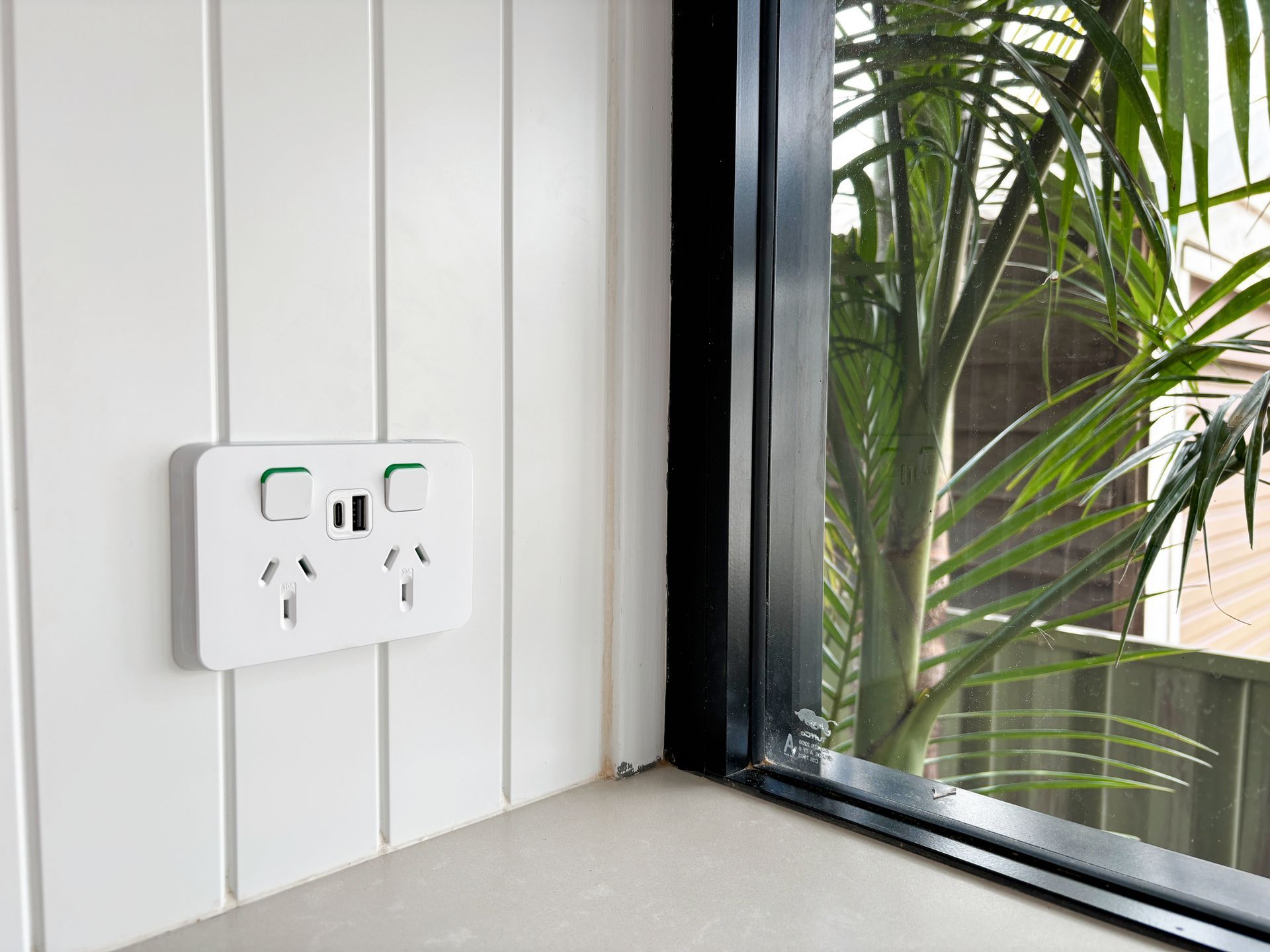 A white electrical outlet on a white wall next to a window.