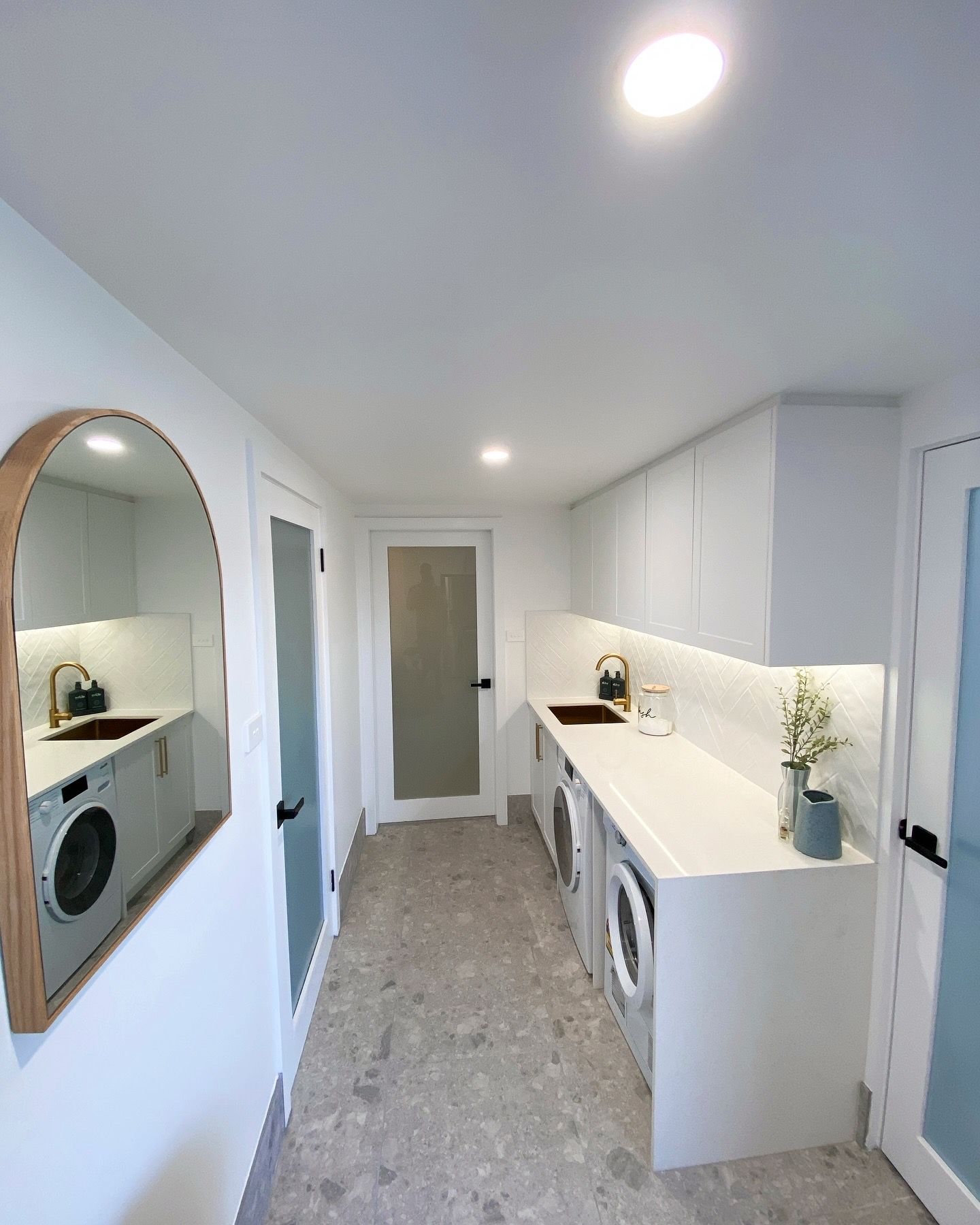A laundry room with a washer and dryer , sink , mirror and downlights.