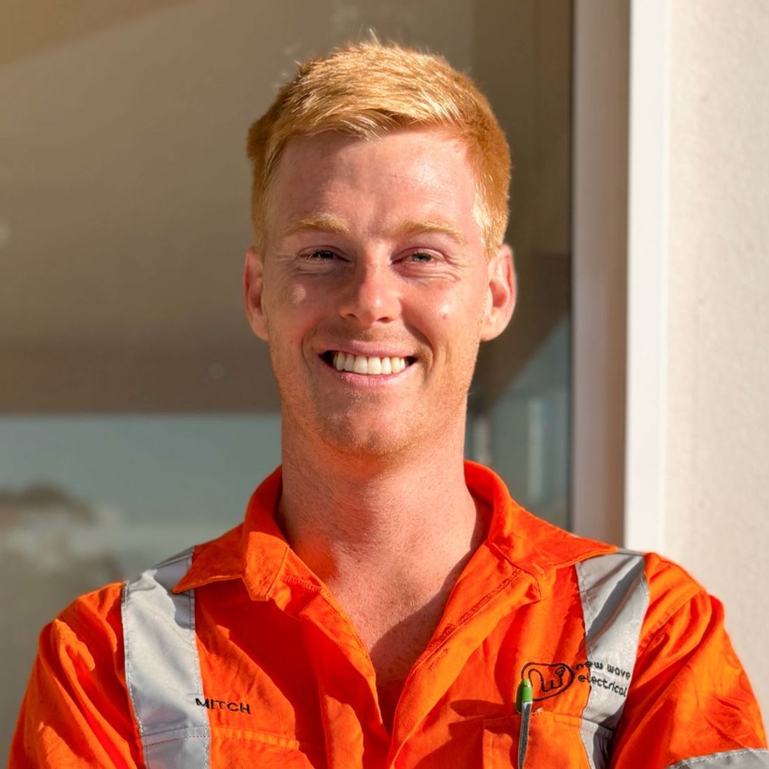 An Electrician smiling man wearing an orange shirt with the name Mi on it
