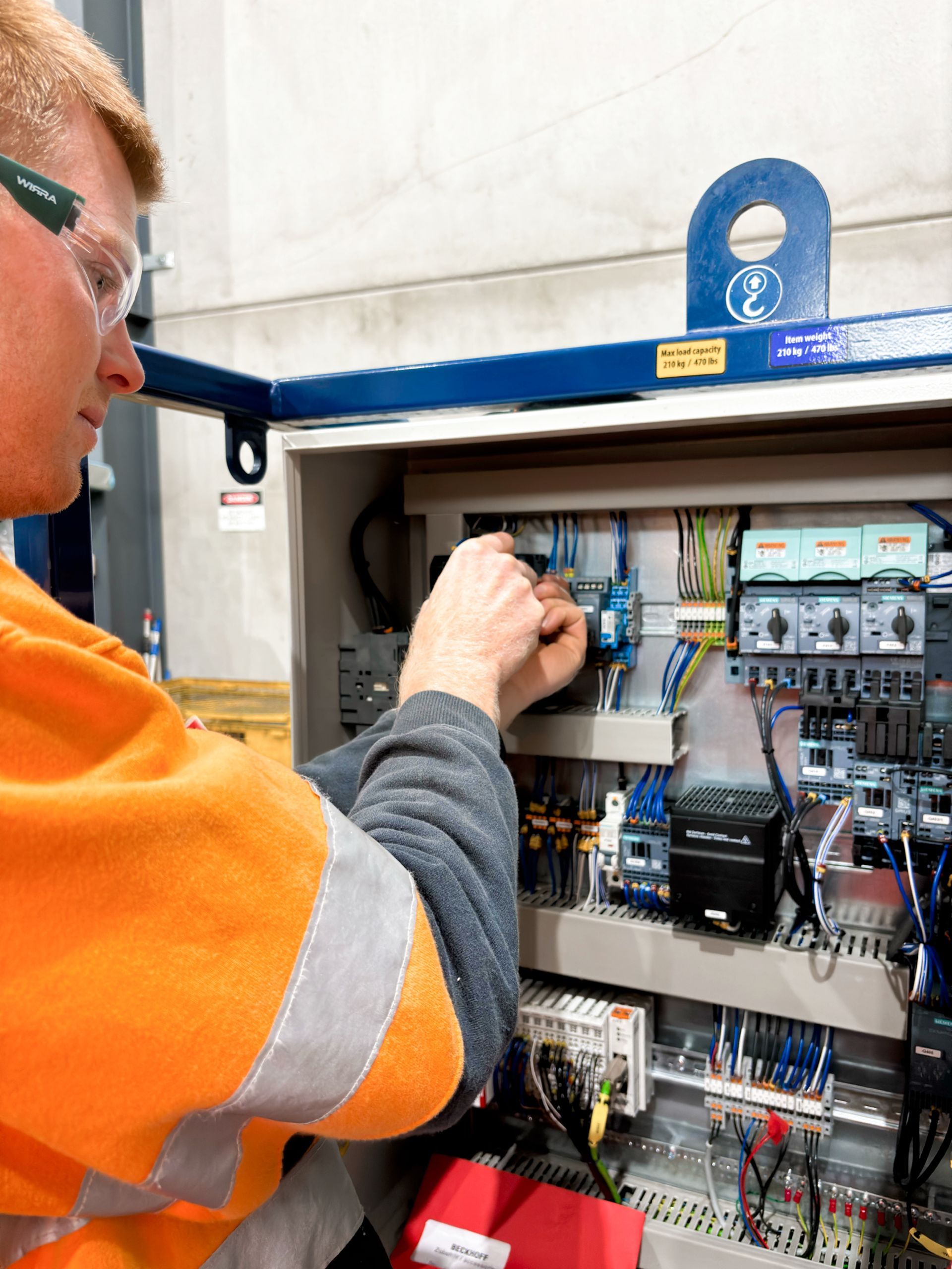 An Electrician wearing safety glasses is working on an electrical switch box .