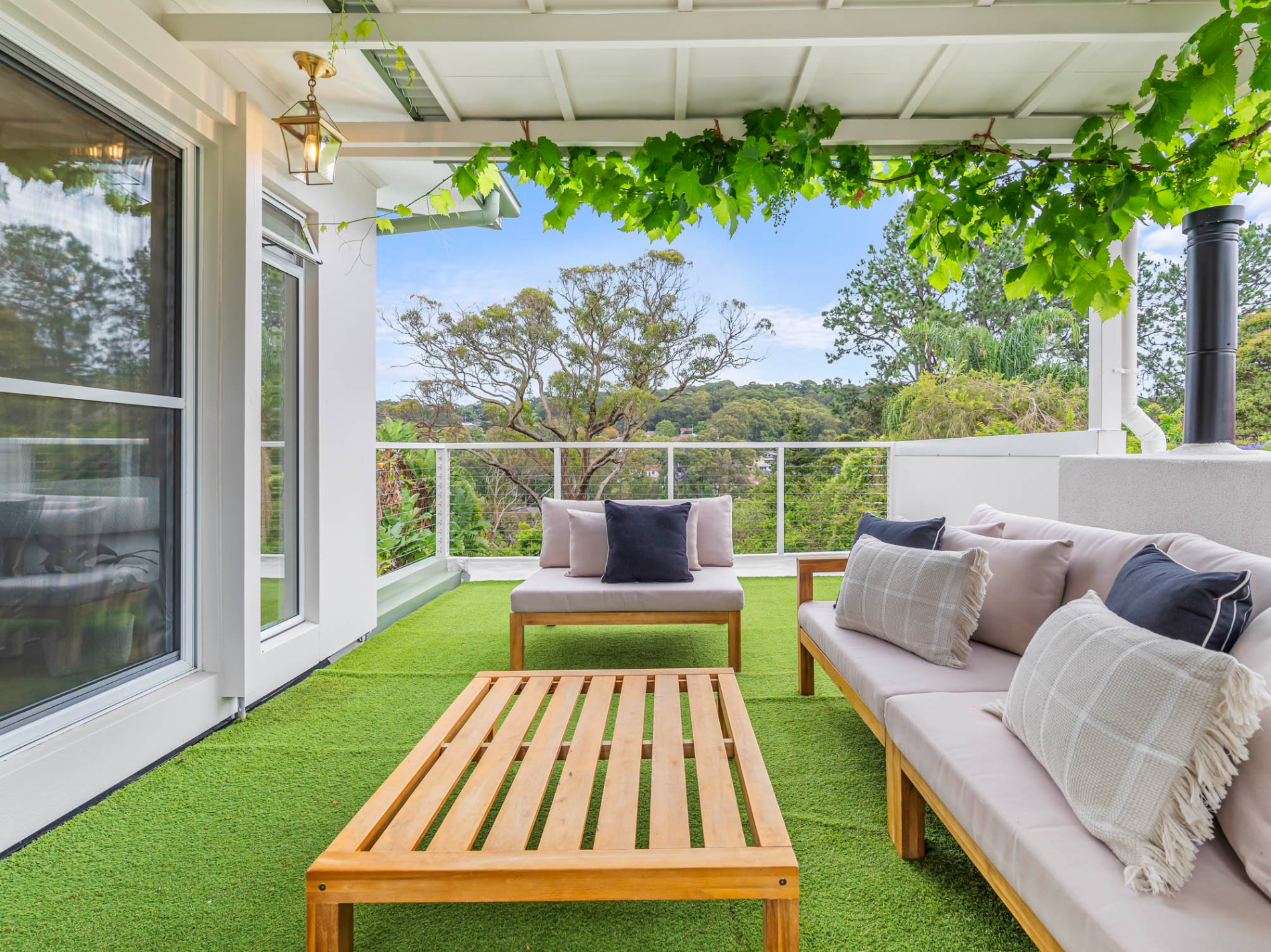 There is a patio with a couch, outdoor wall pendant and a table on it.