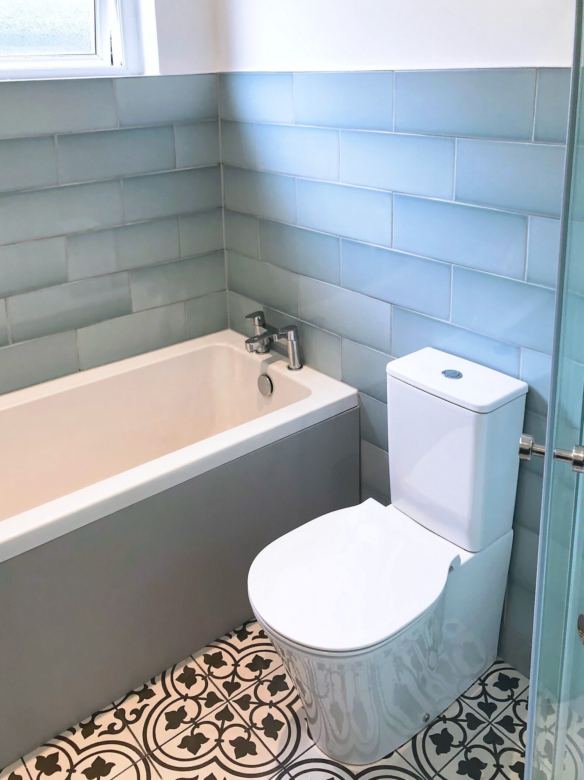 A bathroom with a toilet , bathtub and blue tiles.