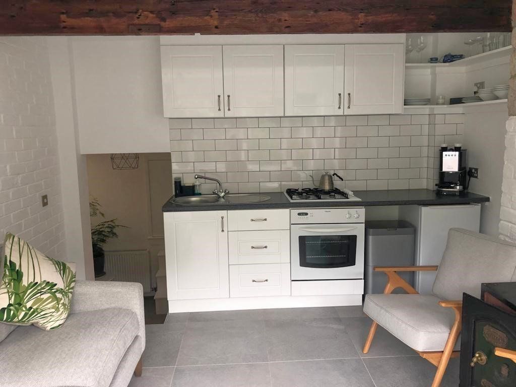 A kitchen with white cabinets , a stove , a sink , and a chair.