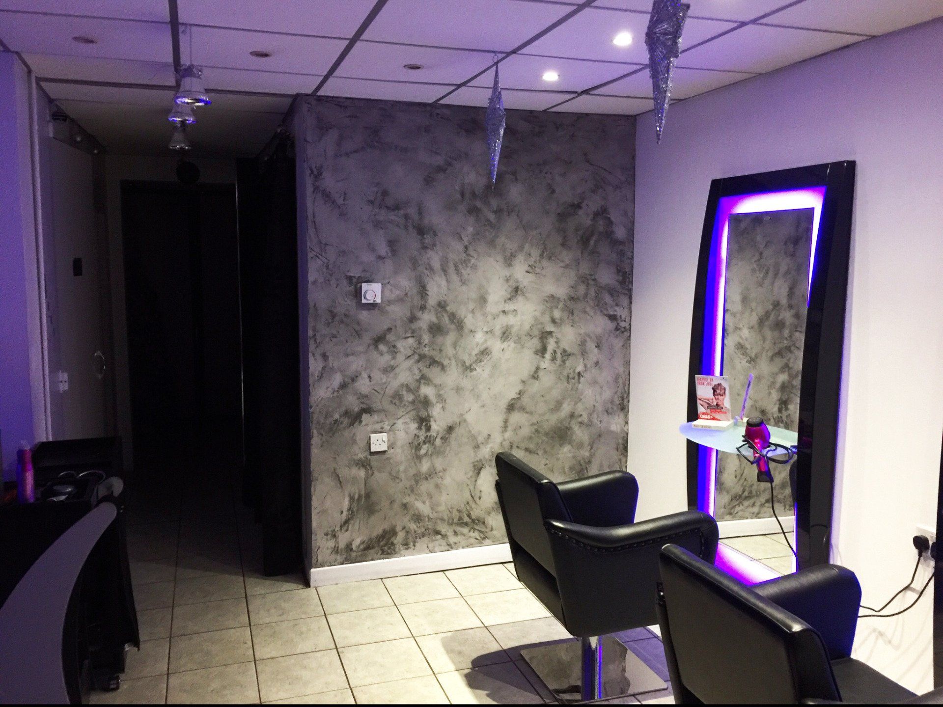A hair salon with two chairs and a mirror with a venetian washed wall in the background.