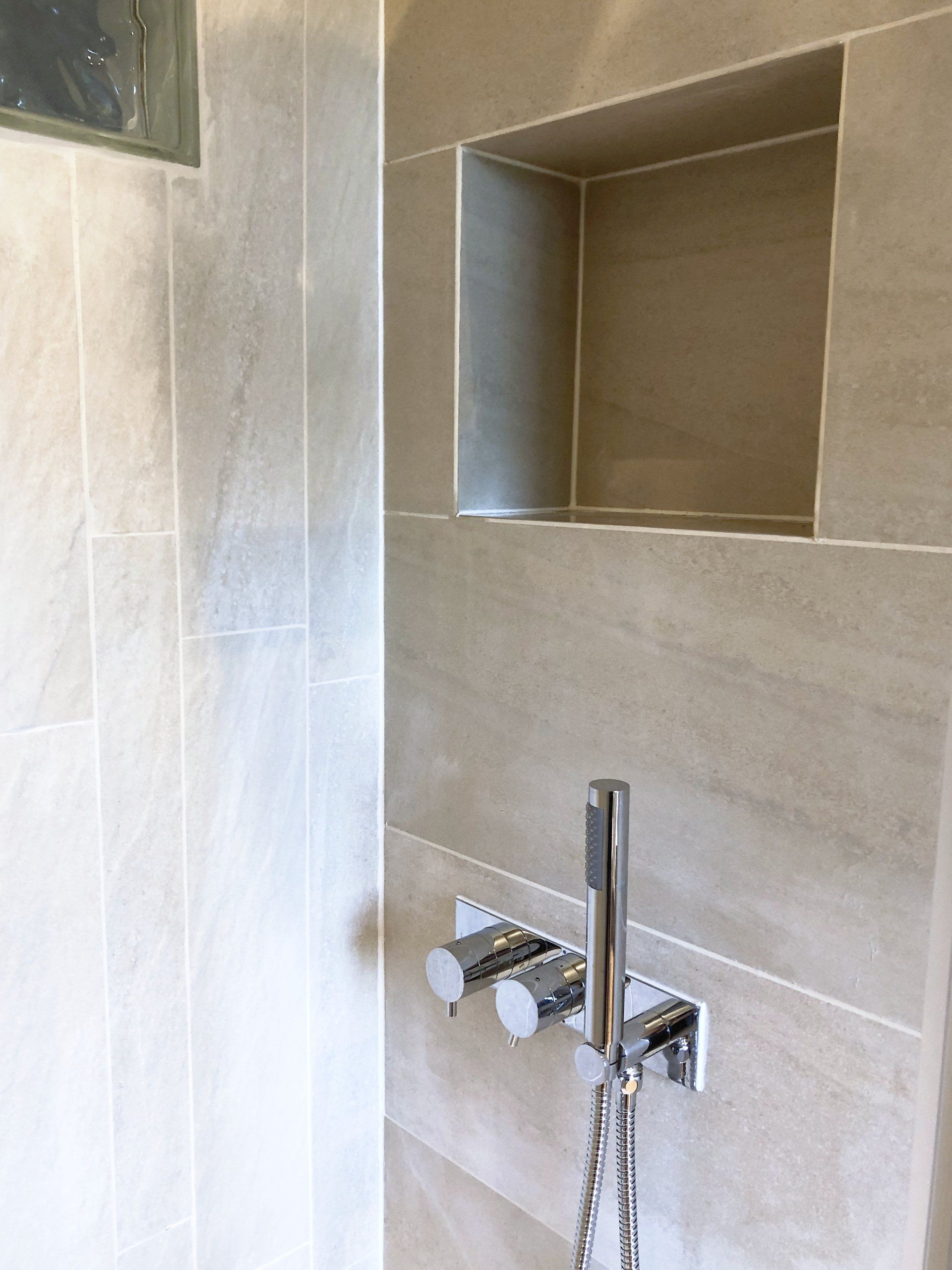 A bathroom with a shower head and a shelf on the wall.
