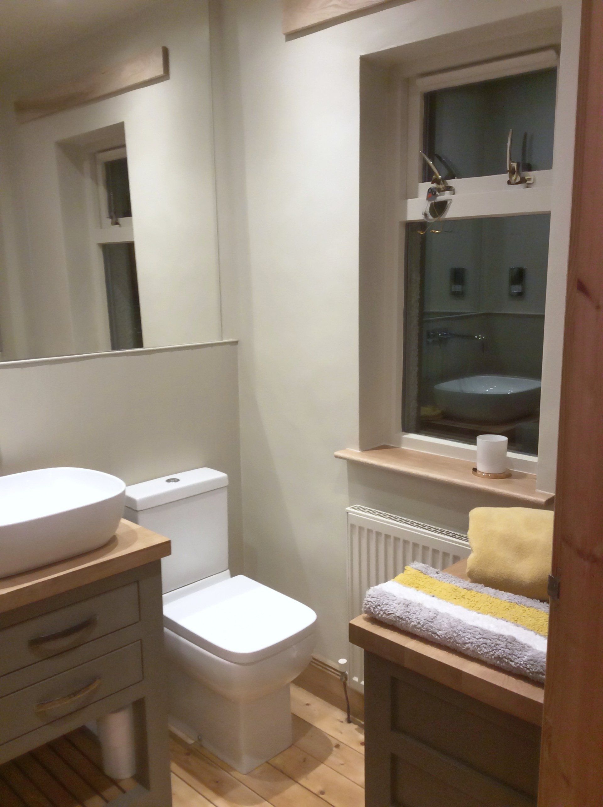 A bathroom with a toilet , sink , mirror and window.