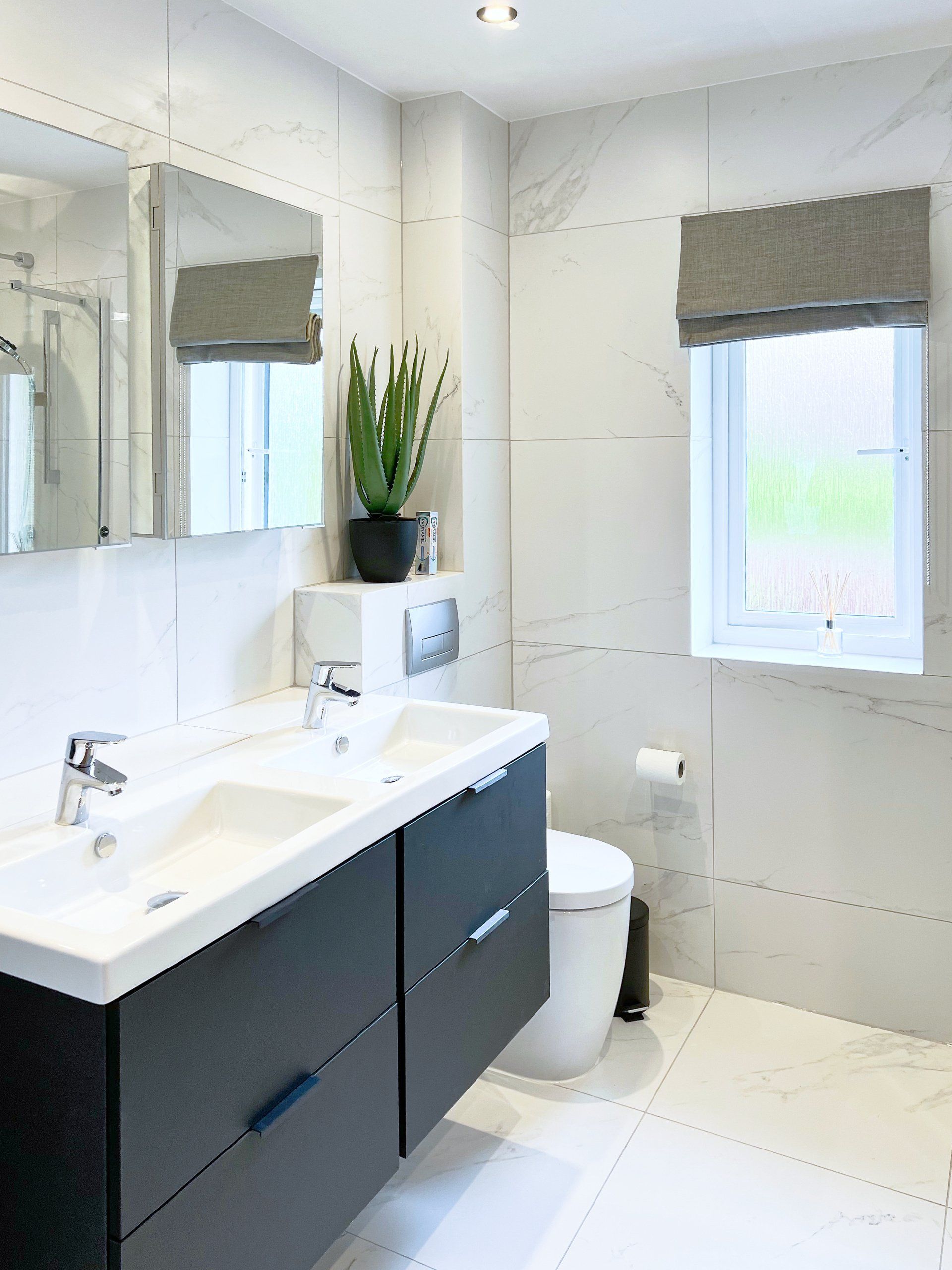 A bathroom with two modern sinks, toilet, mirror and window.