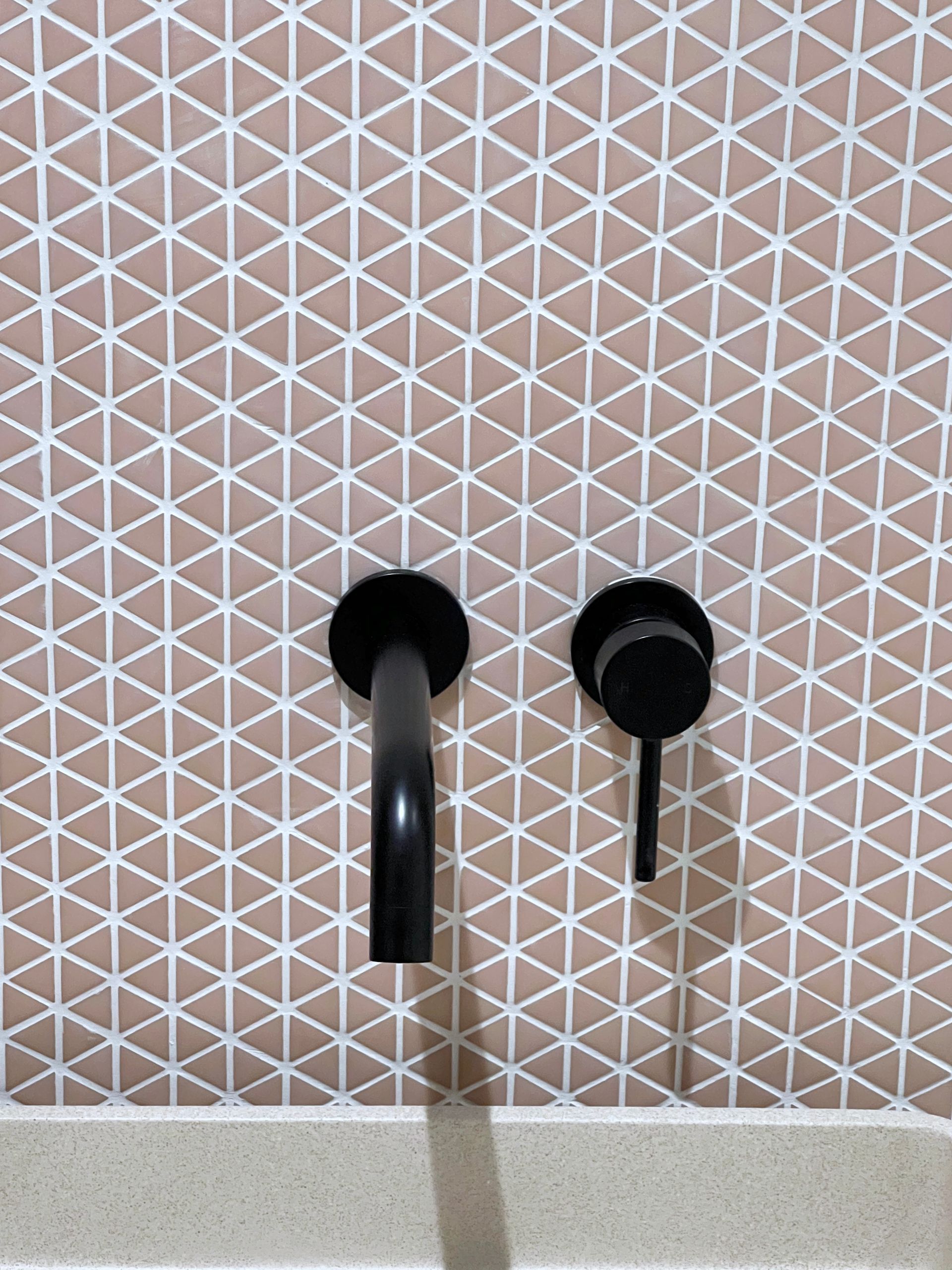 A bathroom sink with two black faucets and a pink tile wall