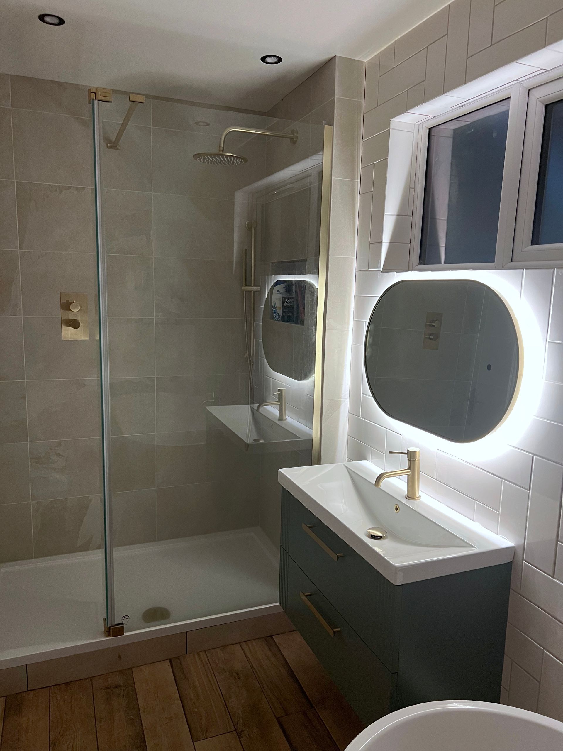 A bathroom with a sink , back-lit mirror and shower seen at night.