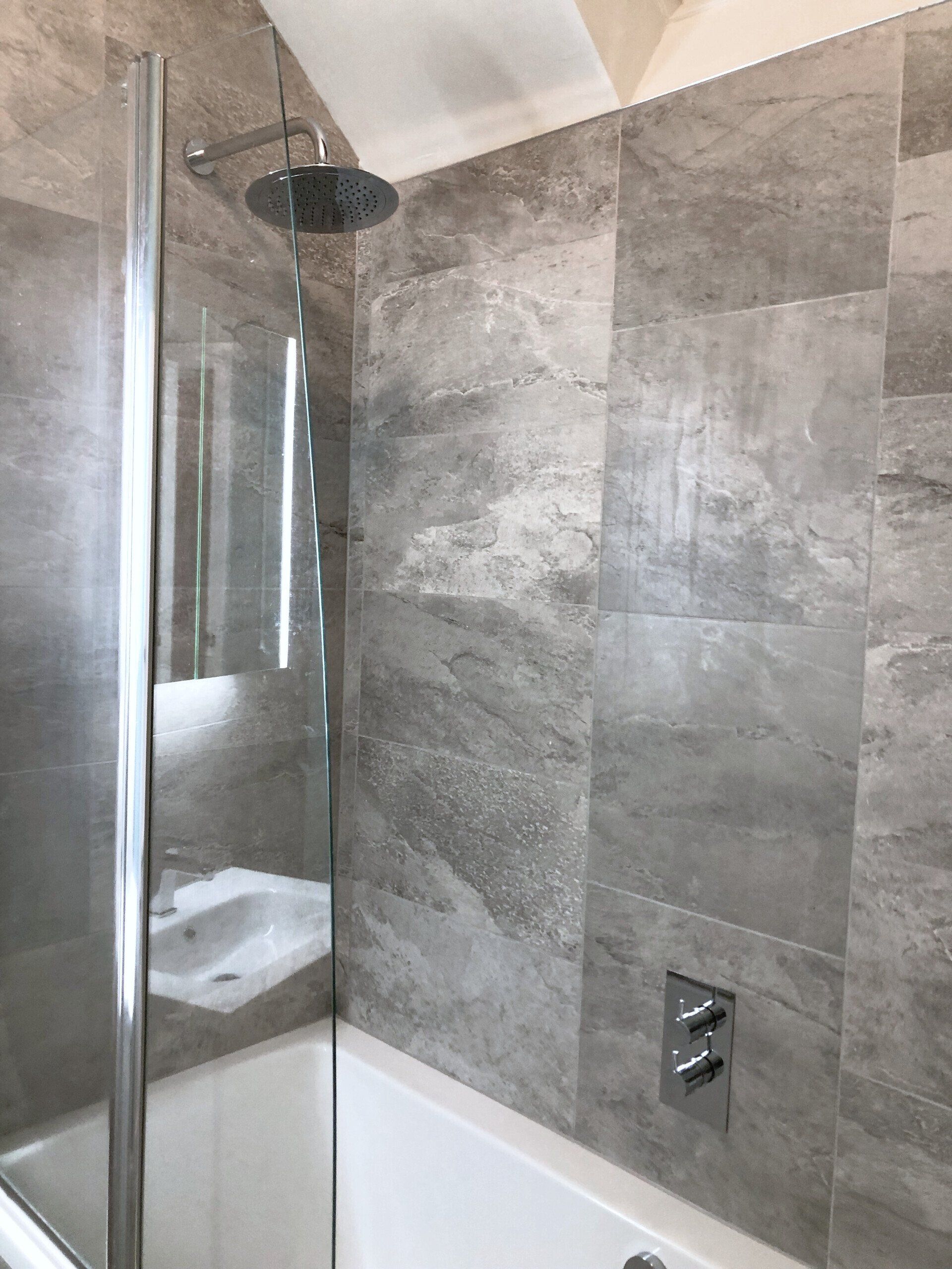 A bathroom with a shower and a bathtub and grey marble style tiles.