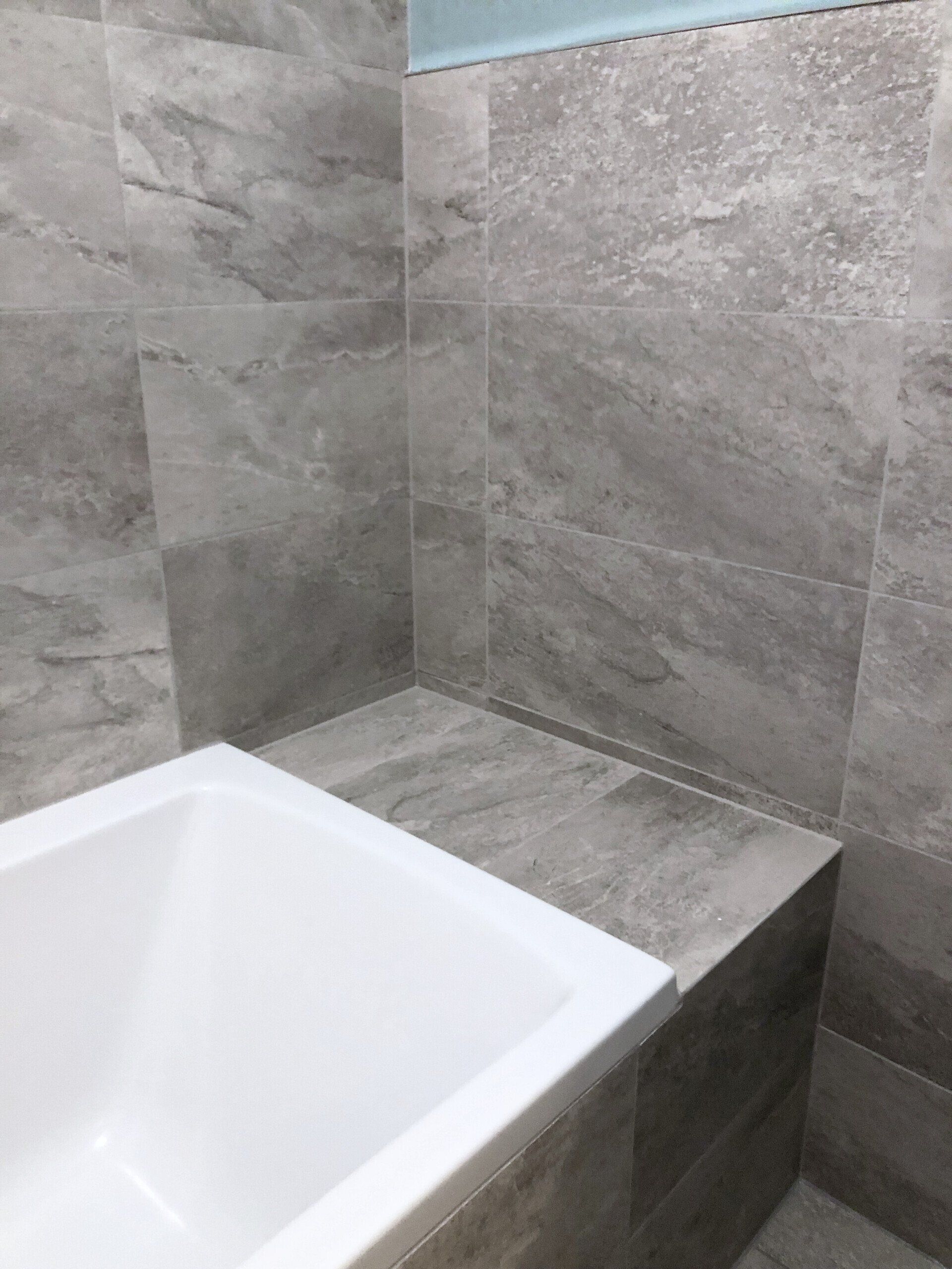 A bathtub in a bathroom with gray tiles on the walls.