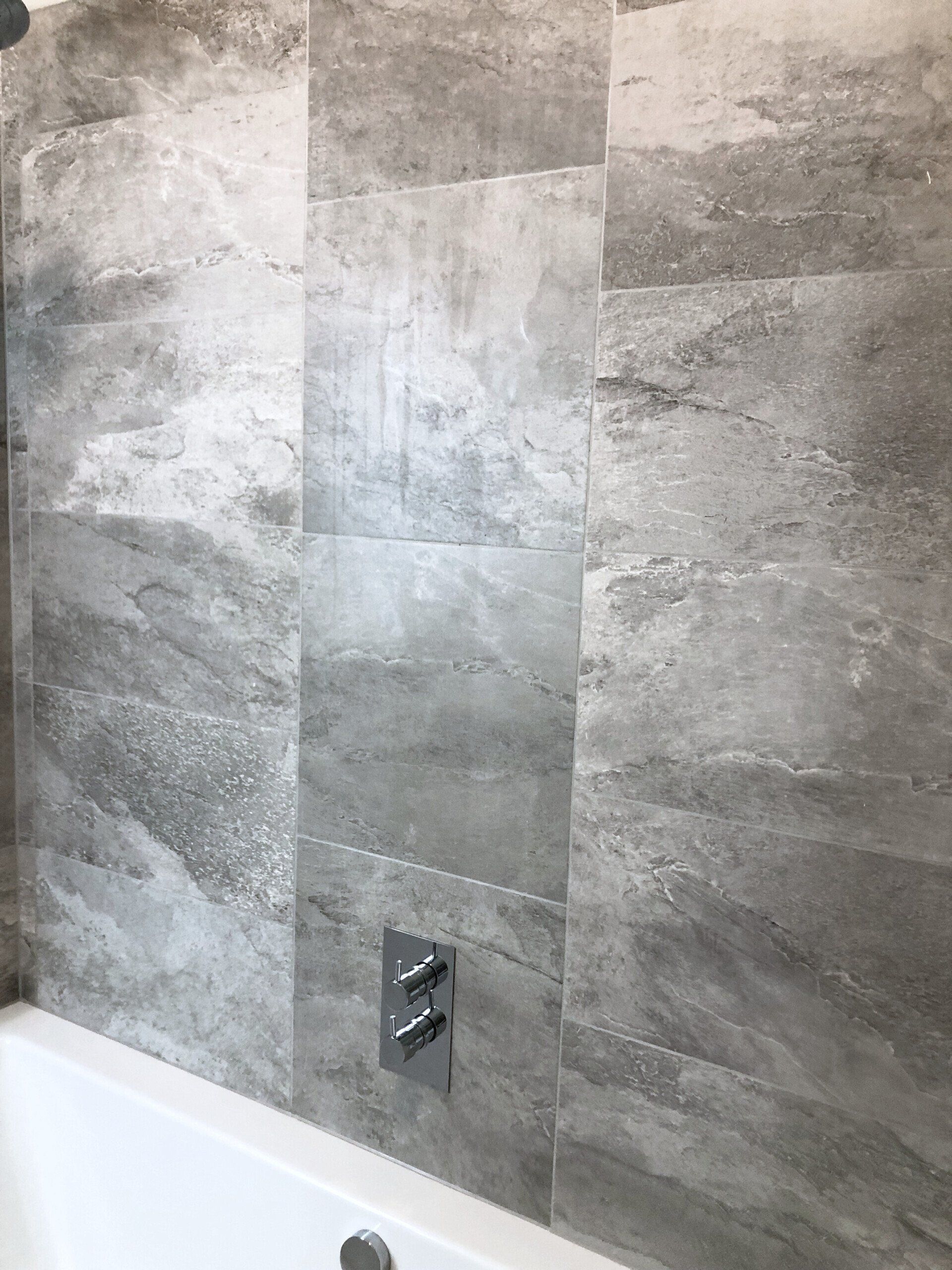 A bathroom with grey tiles on the wall and a bathtub.