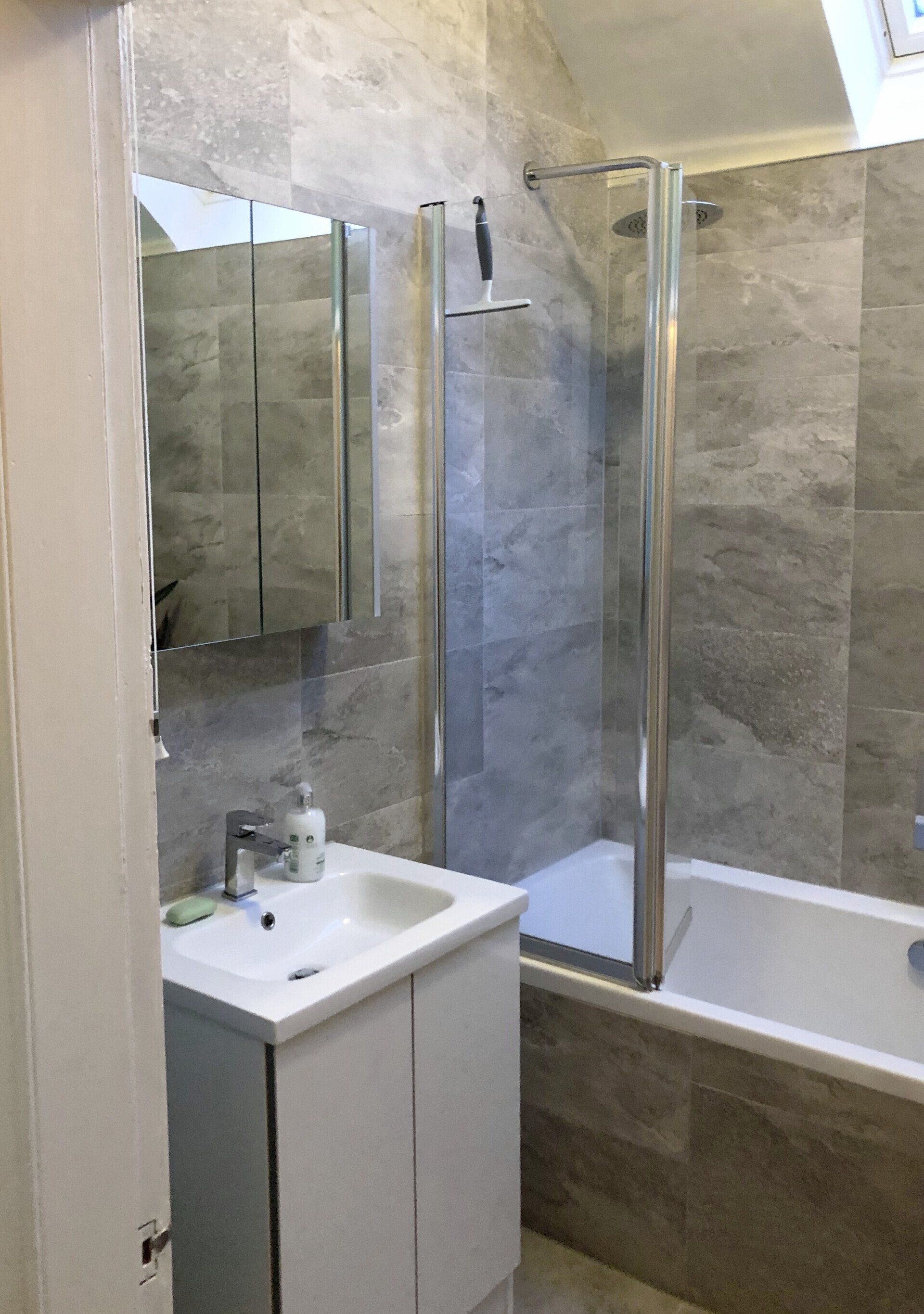 A bathroom with a sink, tub, shower and mirror and grey marble style tiles.