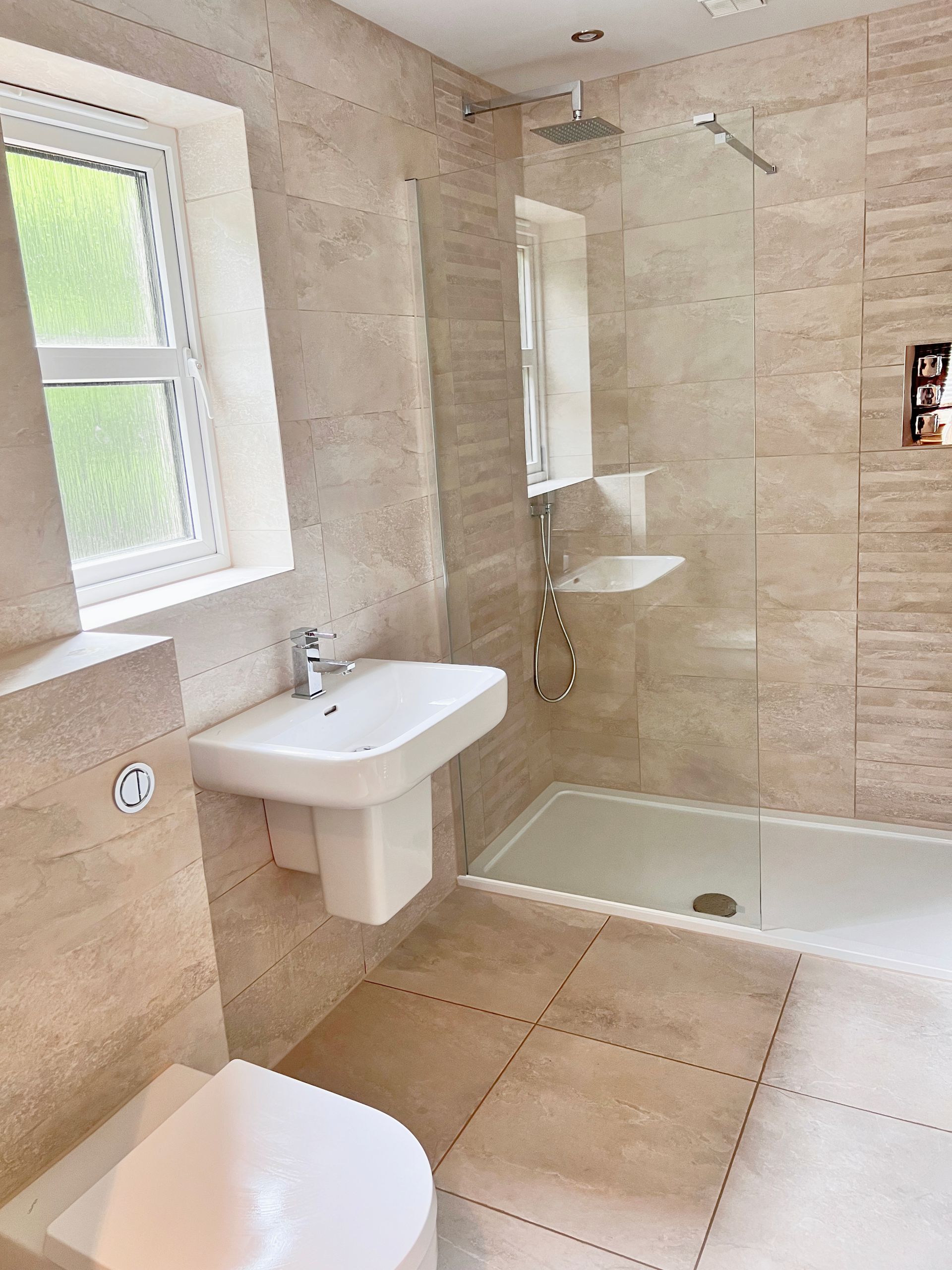 A bathroom with a toilet , sink , shower and window.