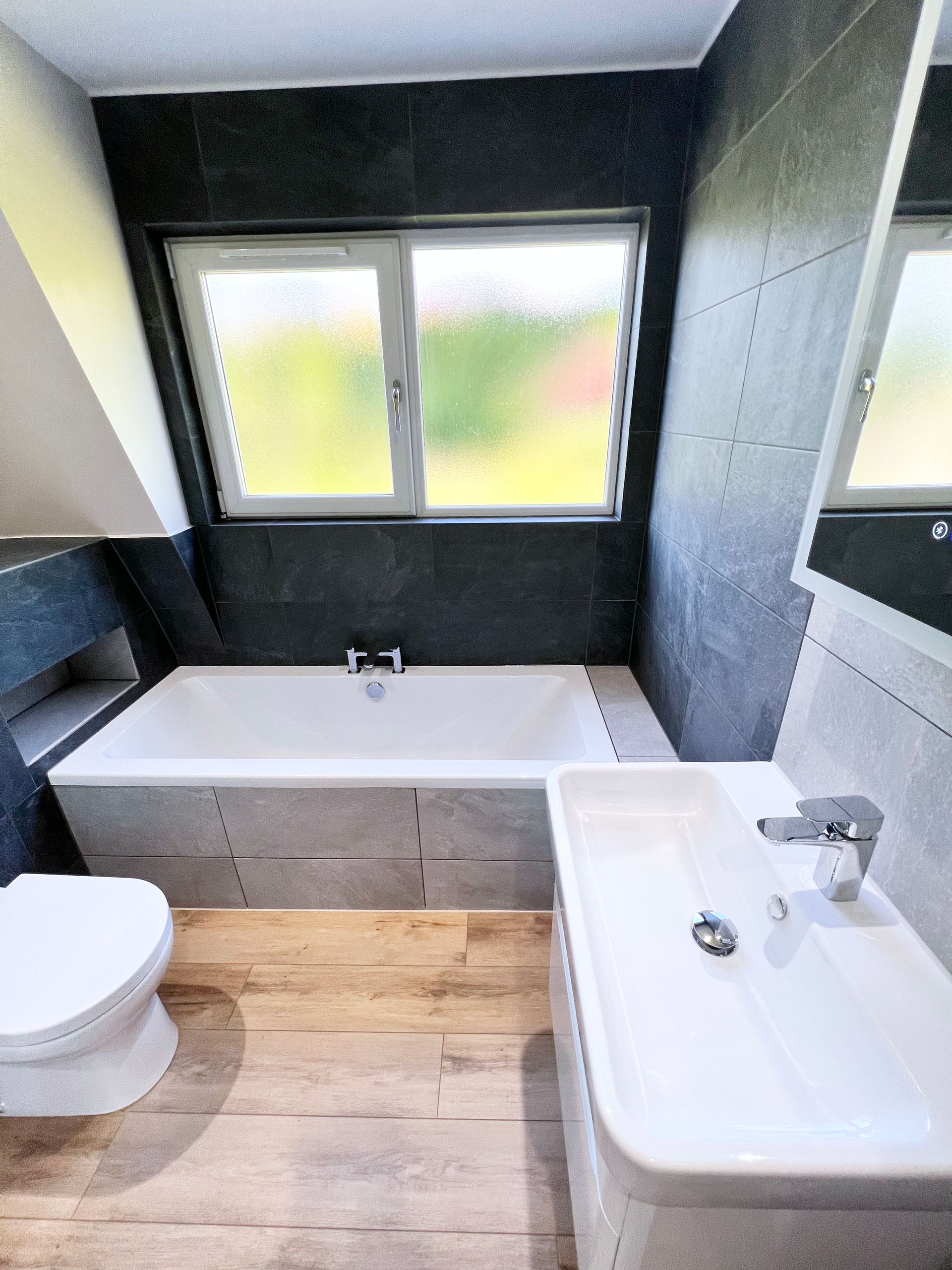 A bathroom with a toilet, sink, bathtub and window.