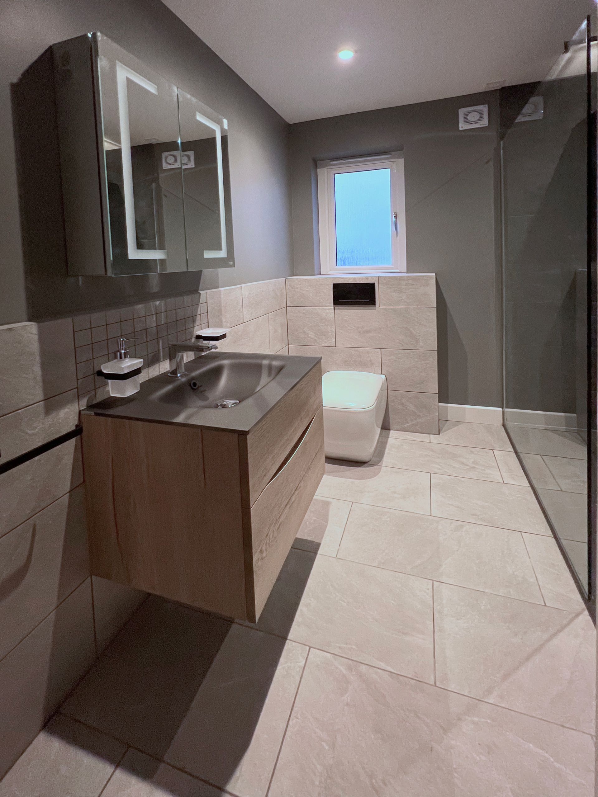 A bathroom with a modern sink, toilet and walk in shower. The tiles are rectangular.