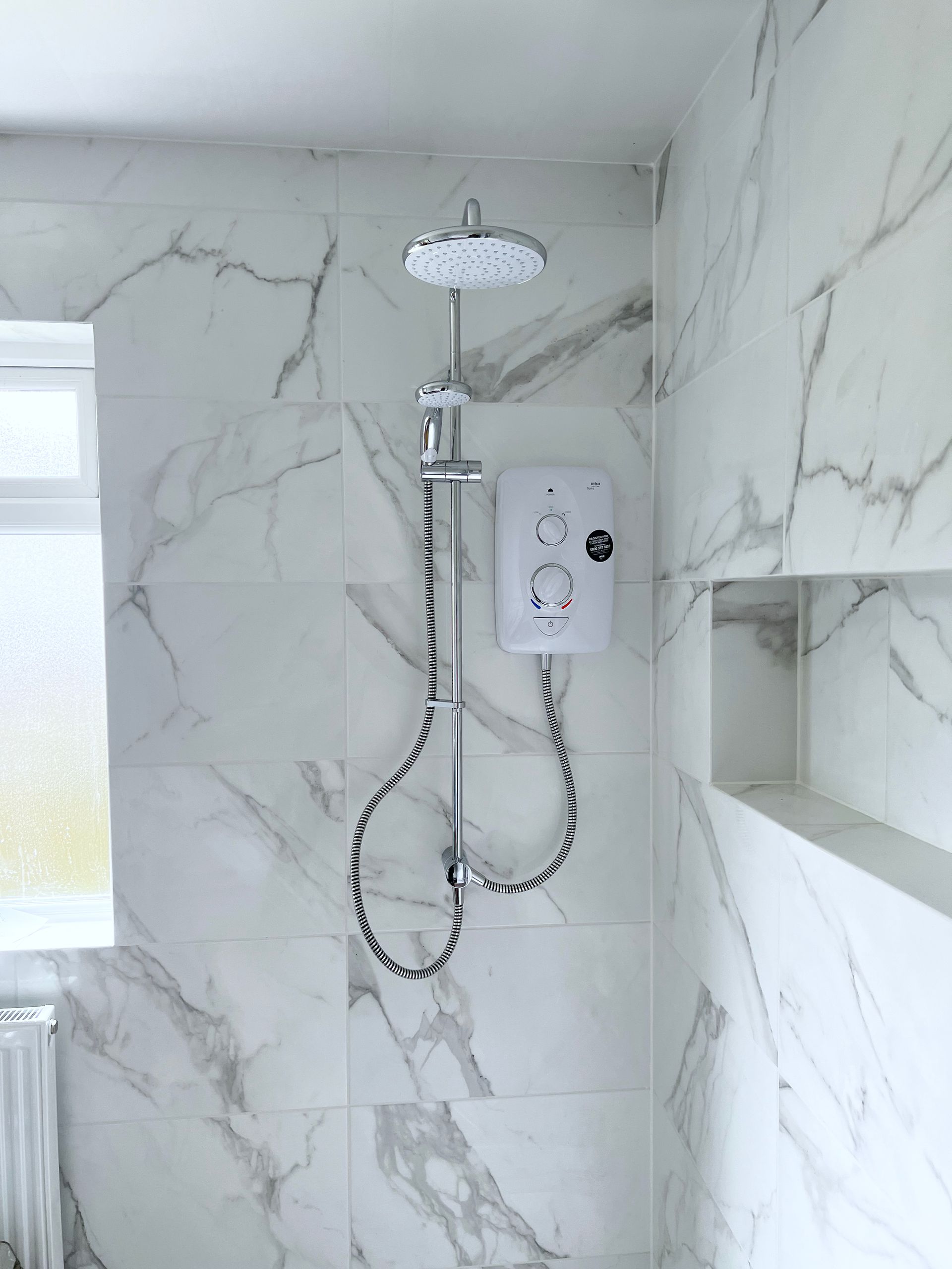 A bathroom with marble tiles and a shower head.