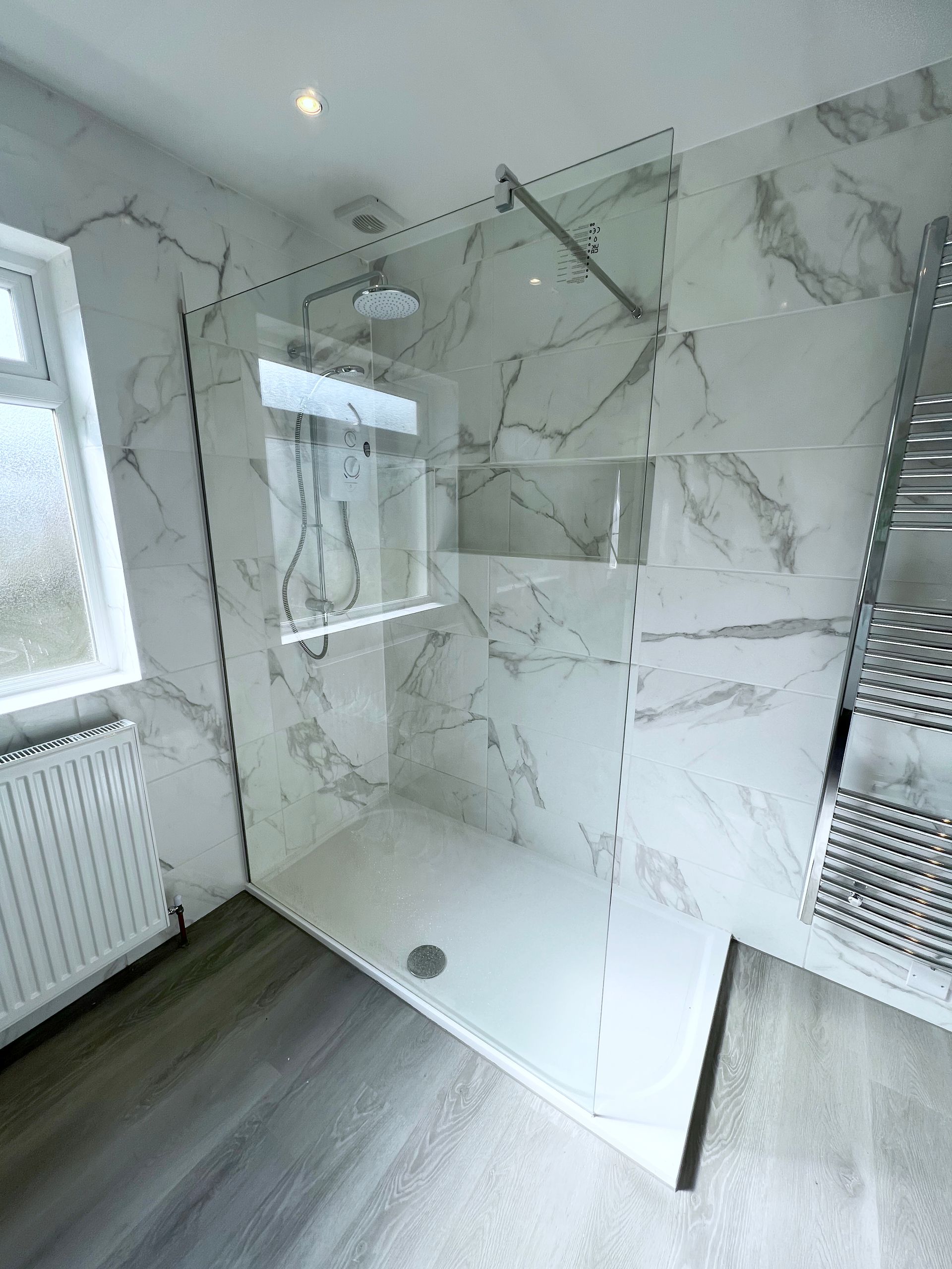 A bathroom with a large walk in shower and marble tiles on the walls.