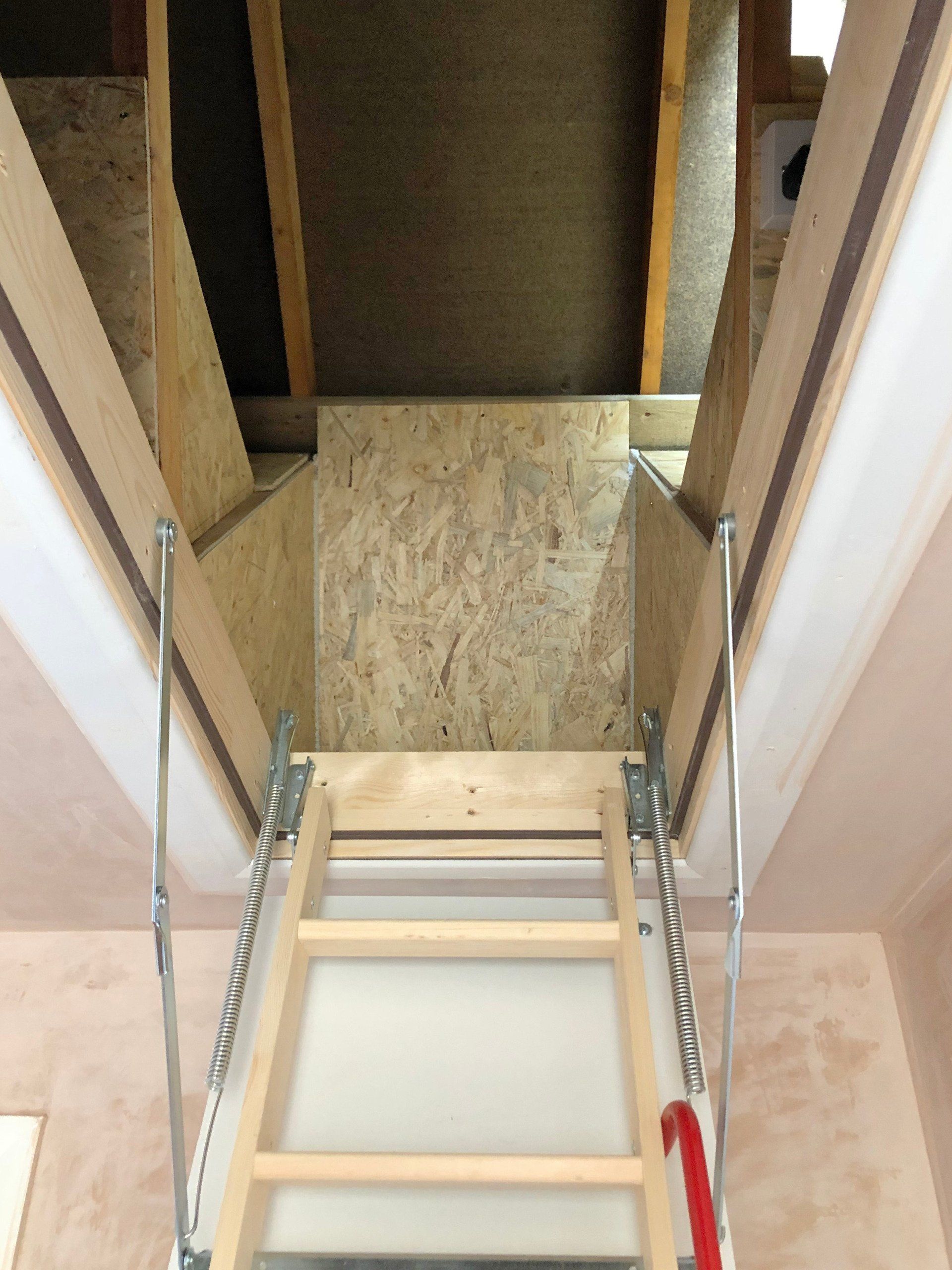 A wooden ladder is leading up to a staircase into the attic. 