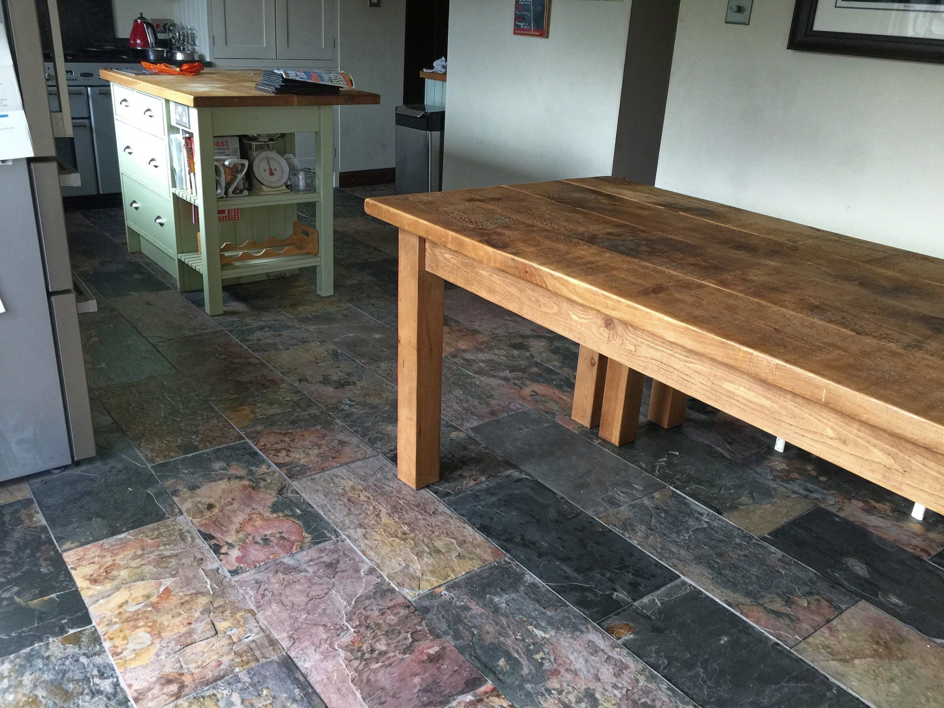A kitchen with natural stone tiled floor and a wooden table and a bench.