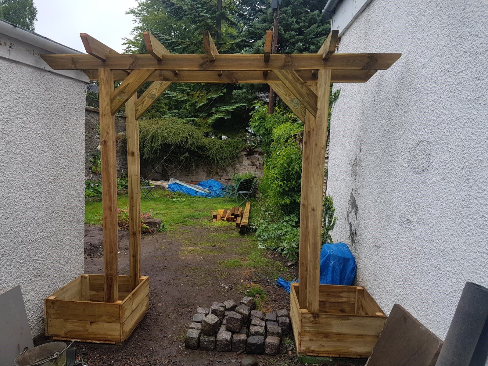 A wooden pergola is being built in a backyard.