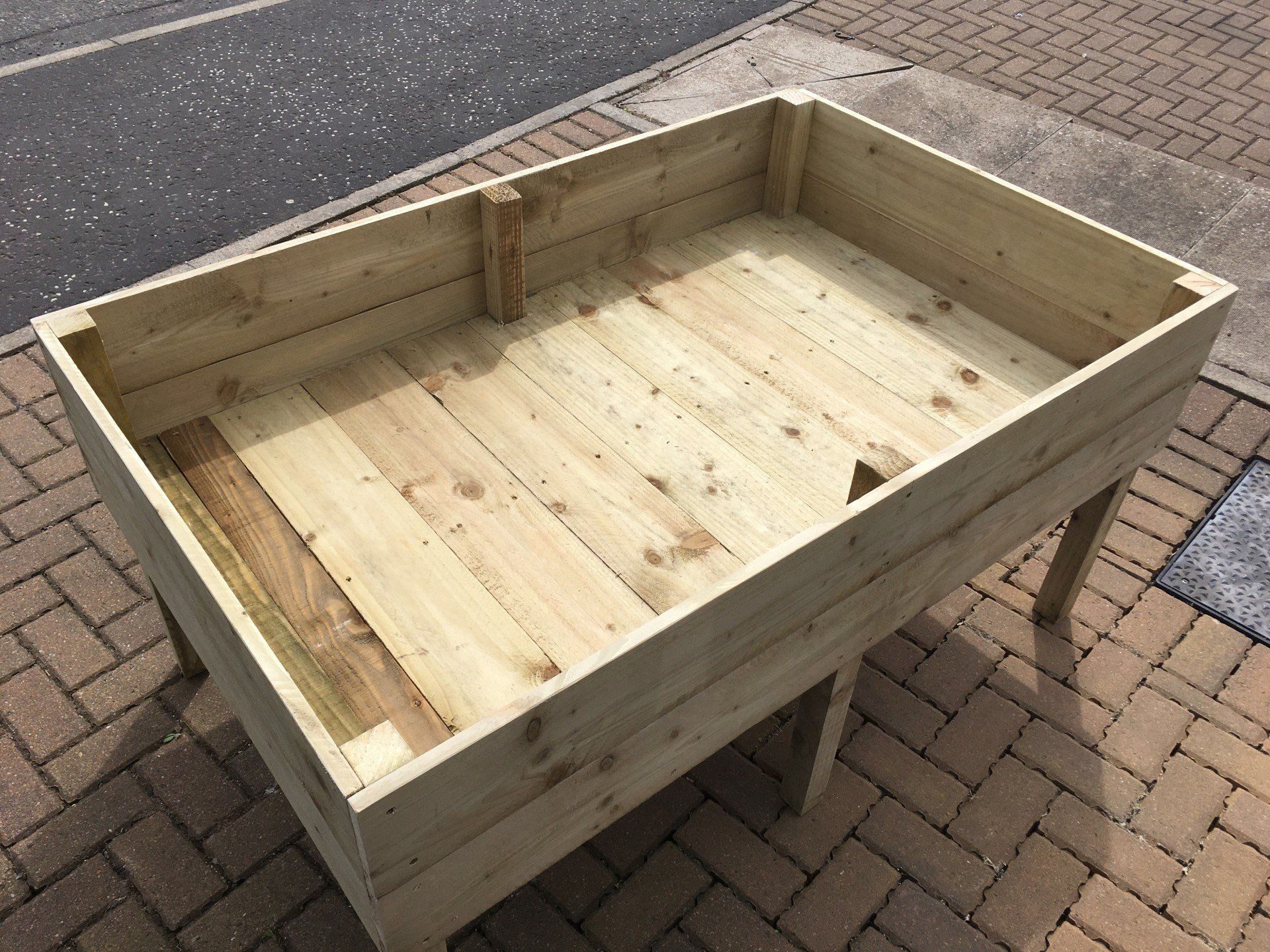 A wooden planter is sitting on a monoblock driveway in front of a house.