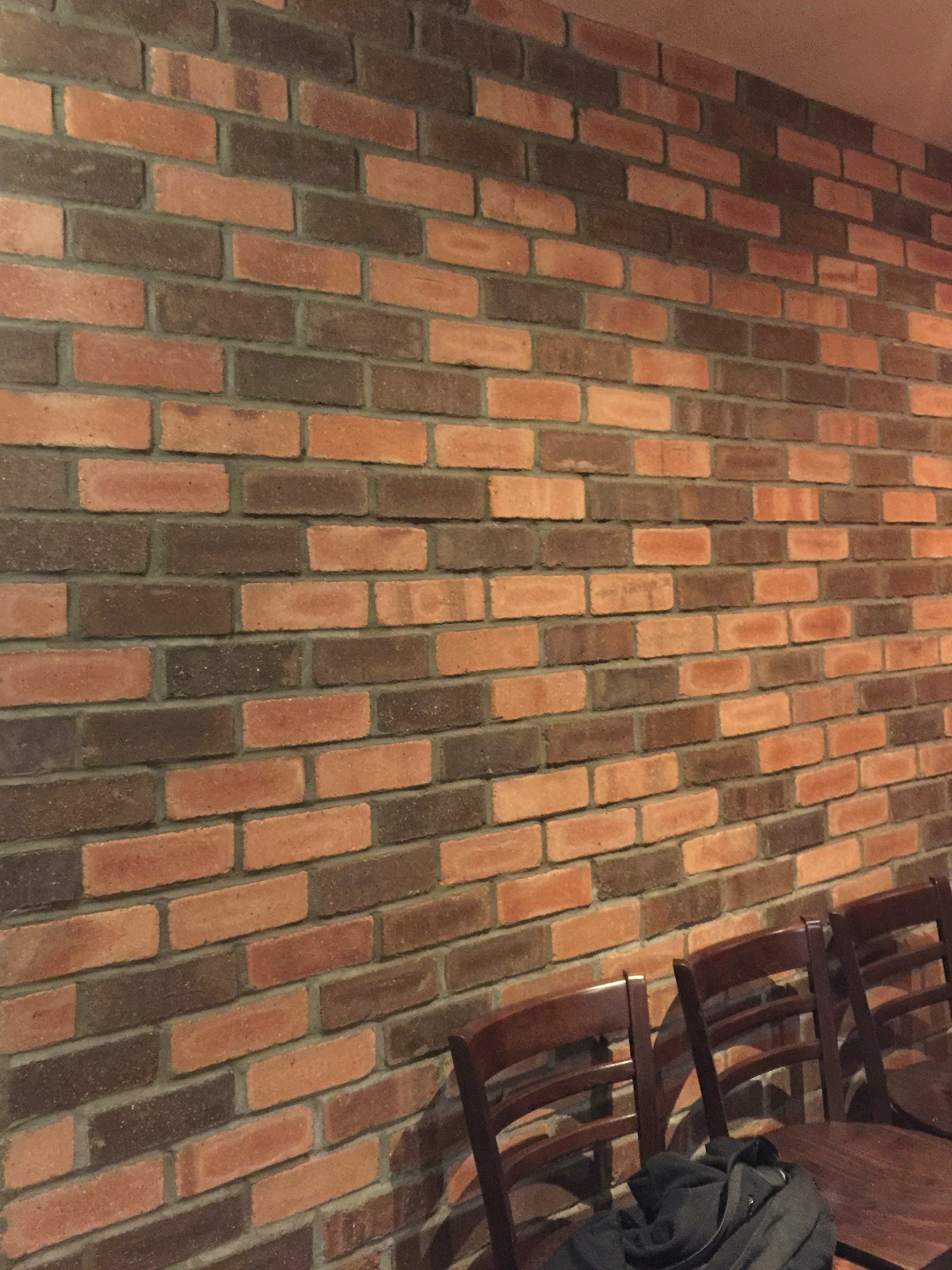 A brick wall with wooden chairs in front of it.