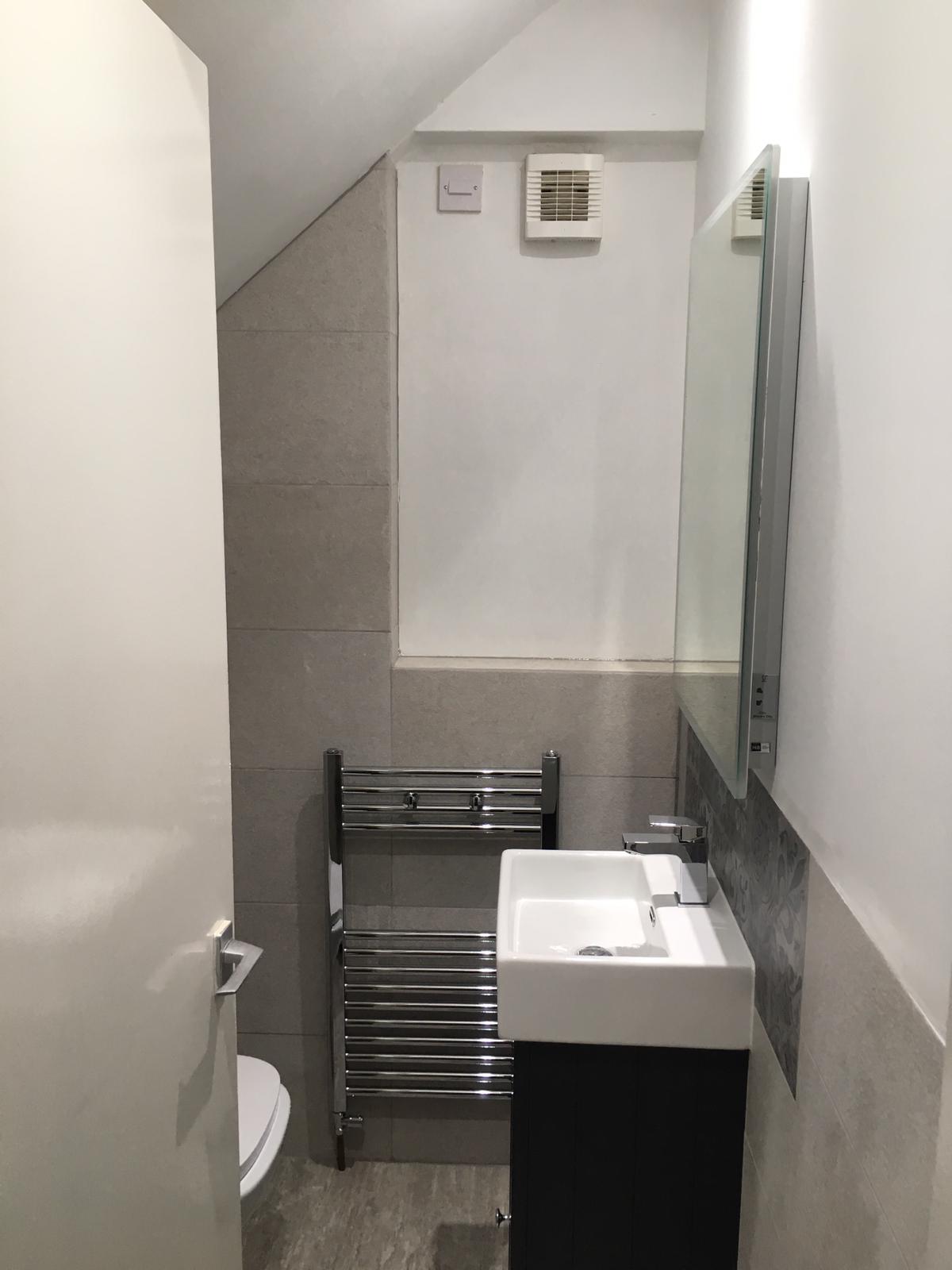 A bathroom with a sink, toilet, mirror and towel rack.